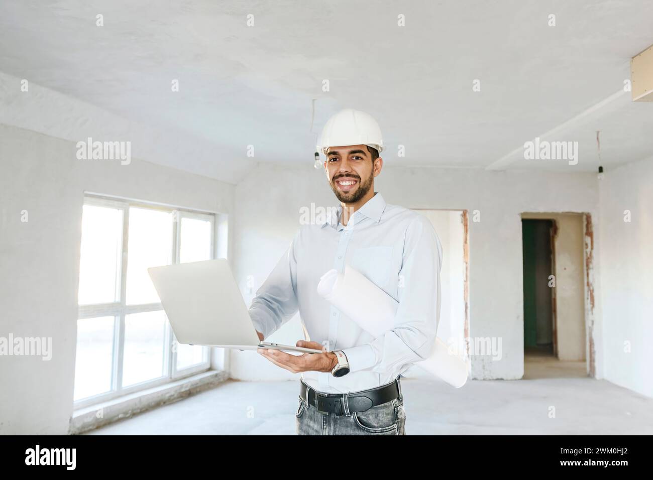 Heureux architecte debout avec plan et ordinateur portable sur le site Banque D'Images