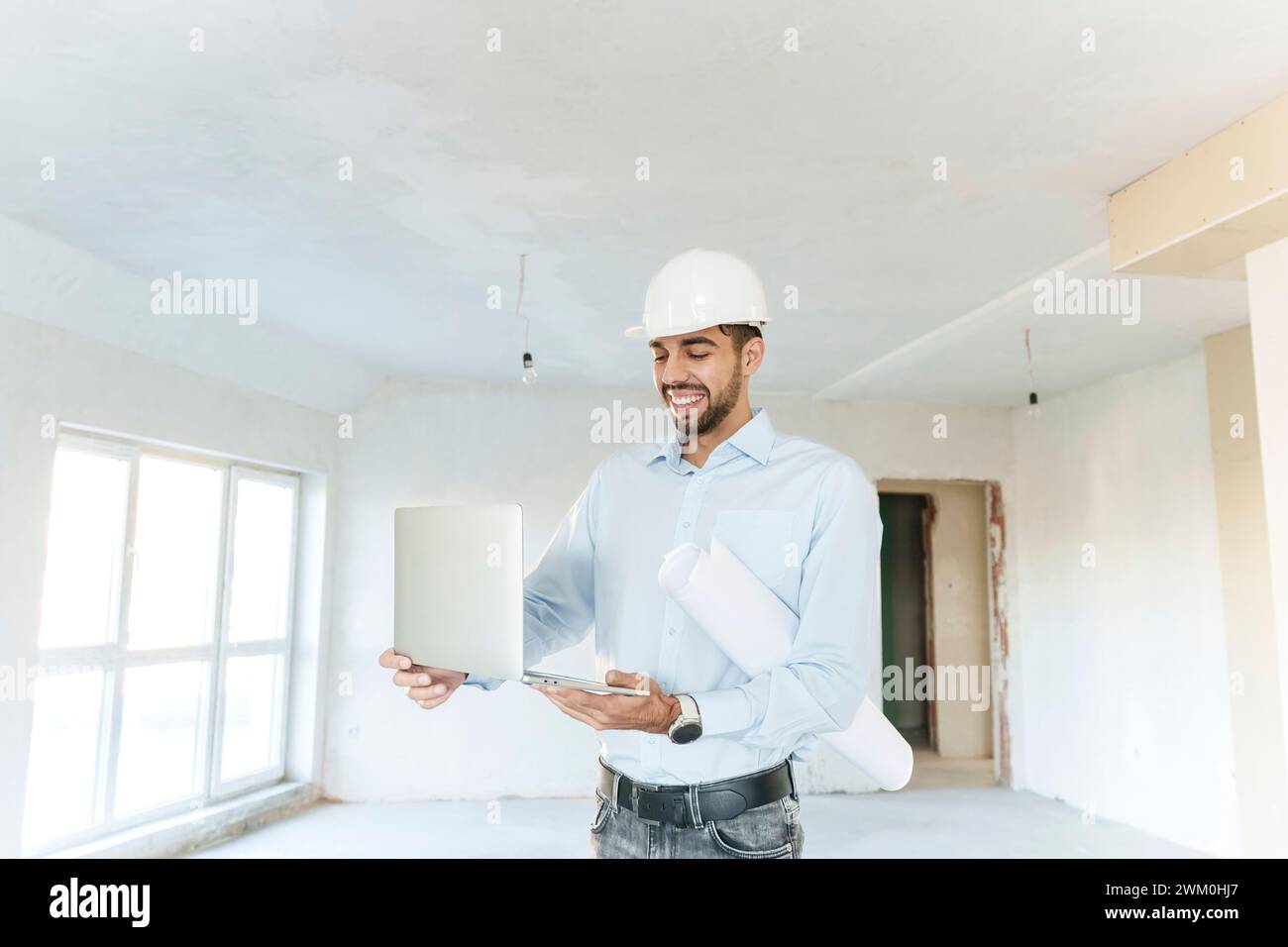 Architecte souriant utilisant un ordinateur portable et tenant le plan sur le site Banque D'Images