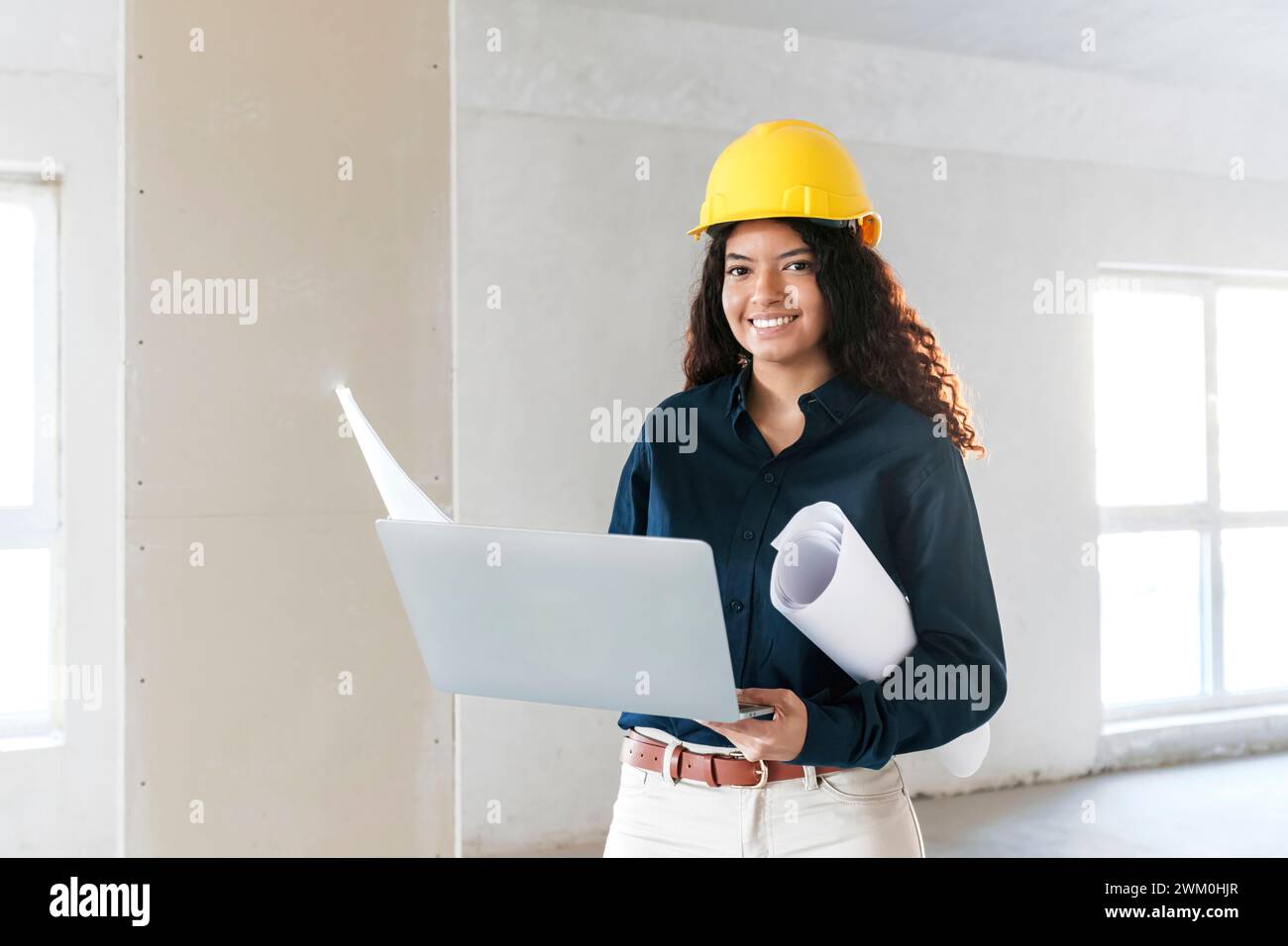 Jeune architecte souriant tenant un ordinateur portable et des plans sur le site Banque D'Images