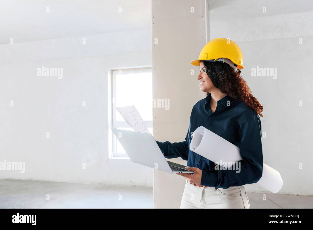 Architecte souriant tenant un ordinateur portable et examinant le site avec des plans Banque D'Images