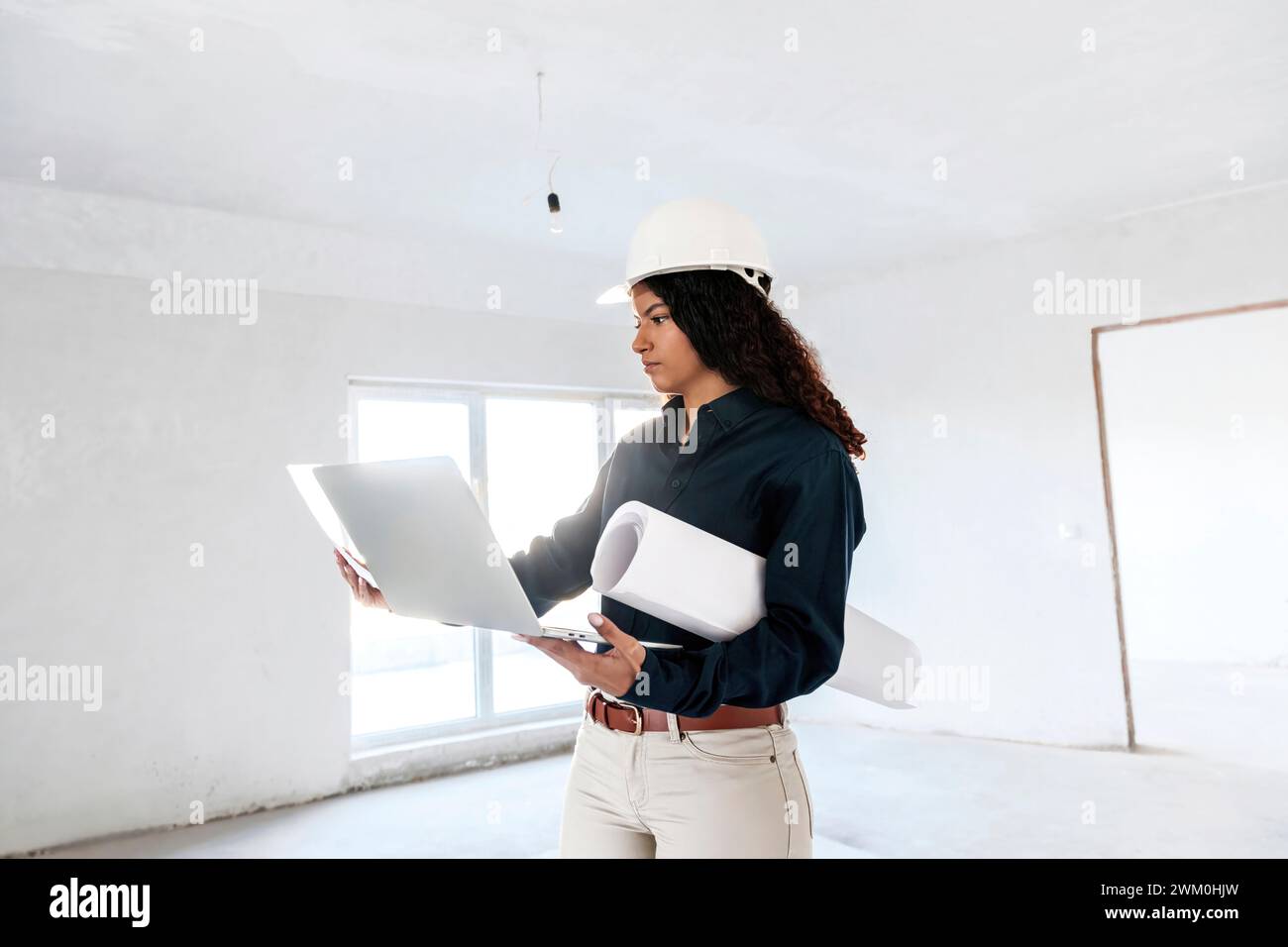 Jeune architecte examinant les plans et debout avec un ordinateur portable sur le site Banque D'Images