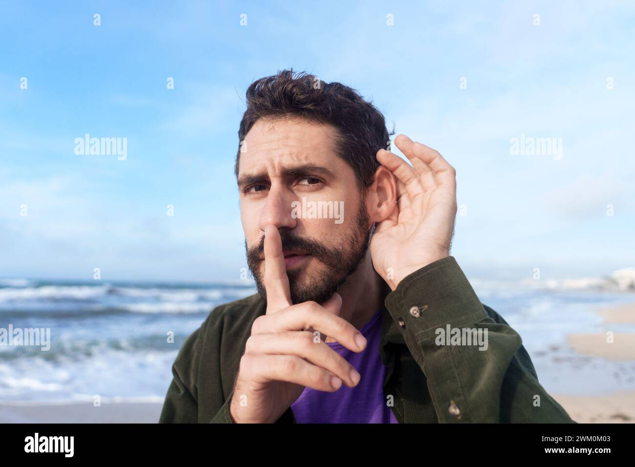Homme espionnage avec le doigt sur les lèvres près de la mer à la plage Banque D'Images