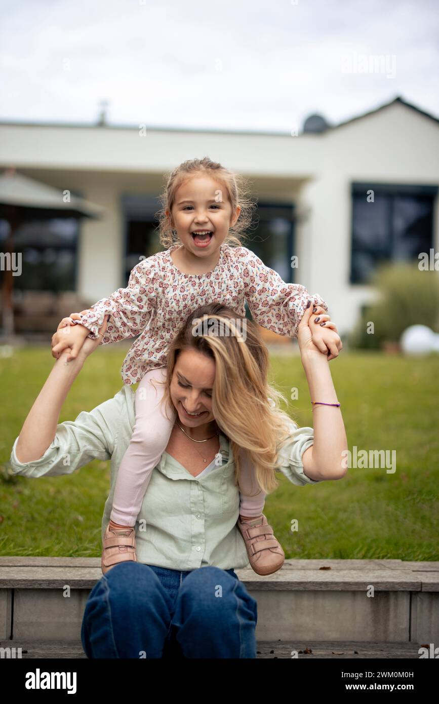 Heureuse mère tenant la main avec la fille assise sur les épaules devant la maison Banque D'Images
