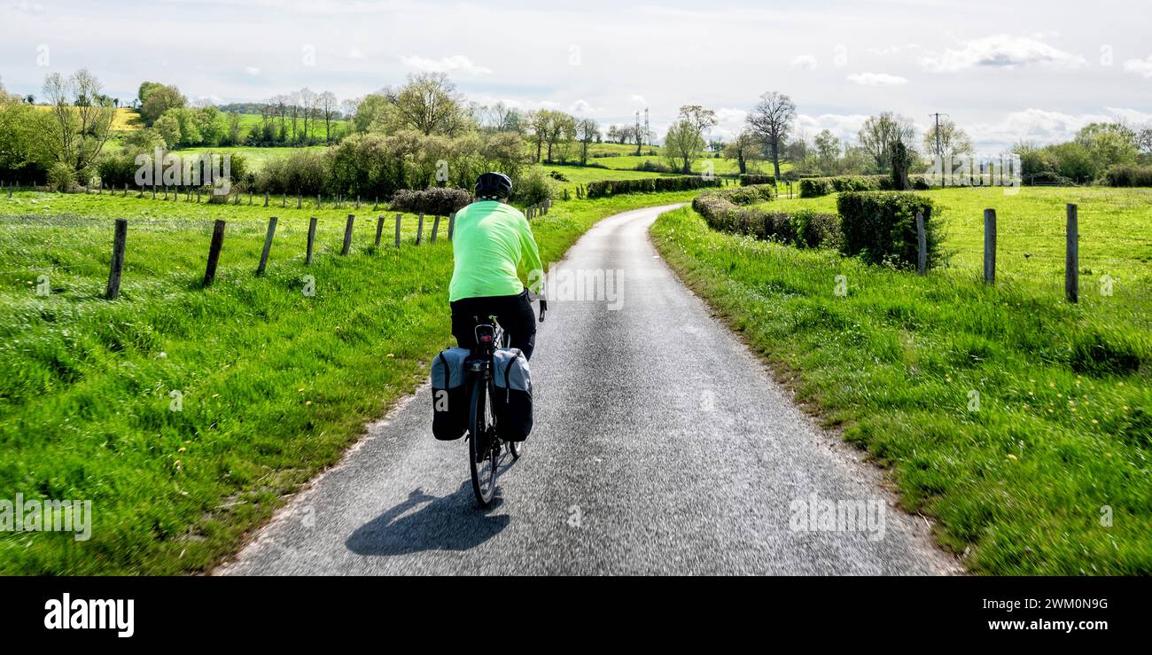 Homme senior cyclant sur la route près du champ le jour ensoleillé Banque D'Images