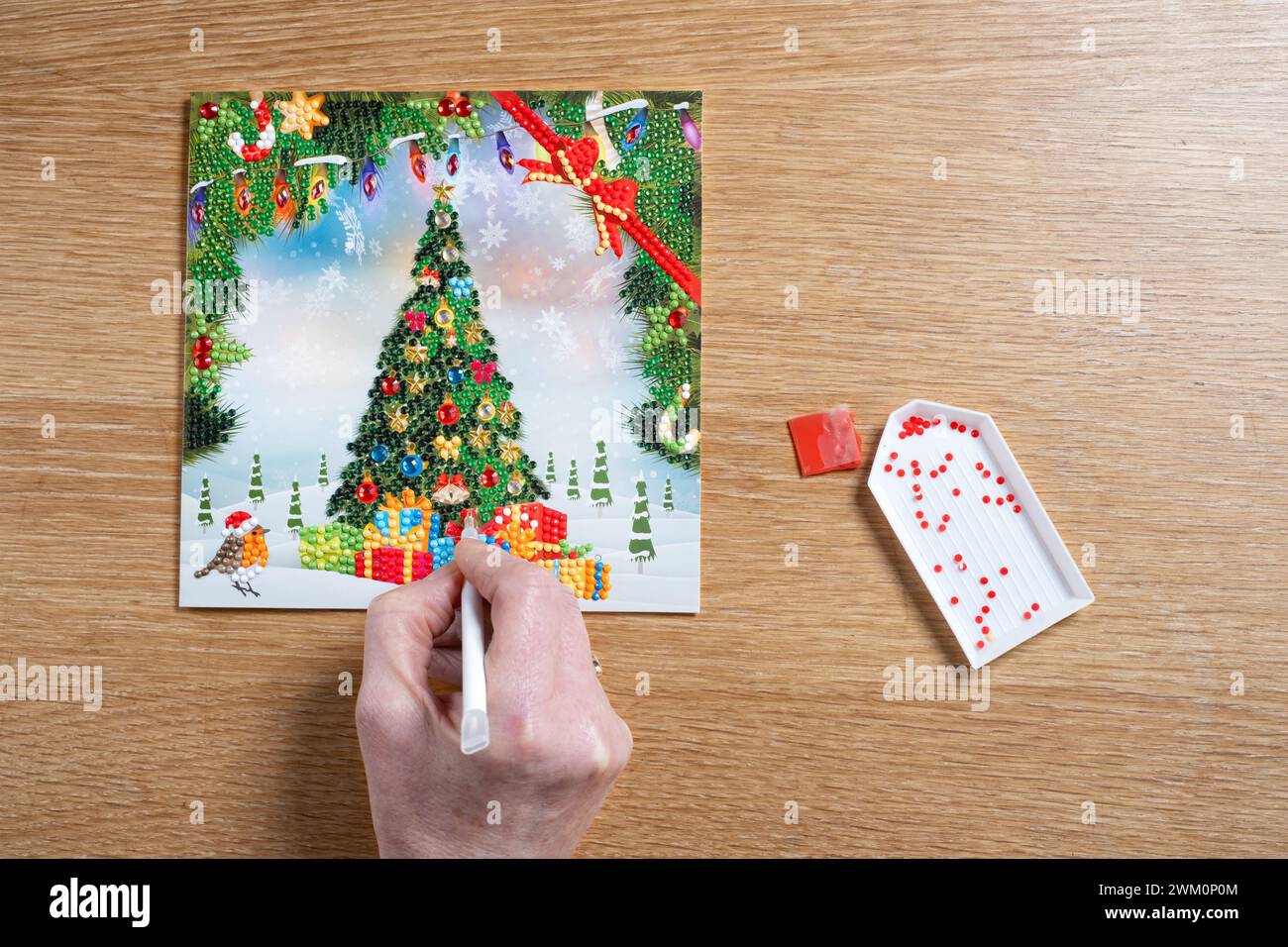 Une femme utilisant un stylo magique pour fixer de petits cristaux ou des diamants à une carte de Noël DIY. Les cristaux colorés sont collés sur une carte adhésive Banque D'Images