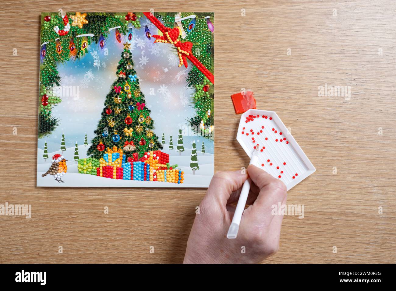 Une femme utilisant un stylo magique pour fixer de petits cristaux ou des diamants à une carte de Noël DIY. Les cristaux colorés sont collés sur une carte adhésive Banque D'Images