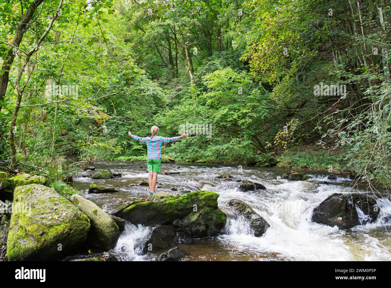 Femme senior baignant dans la forêt avec les bras tendus par le ruisseau Banque D'Images