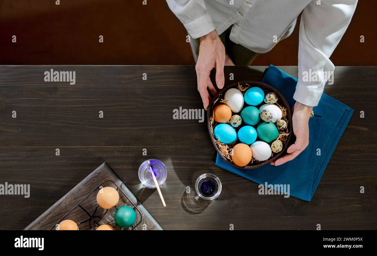 Femme avec panier d'œufs de pâques colorés sur la table à la maison Banque D'Images