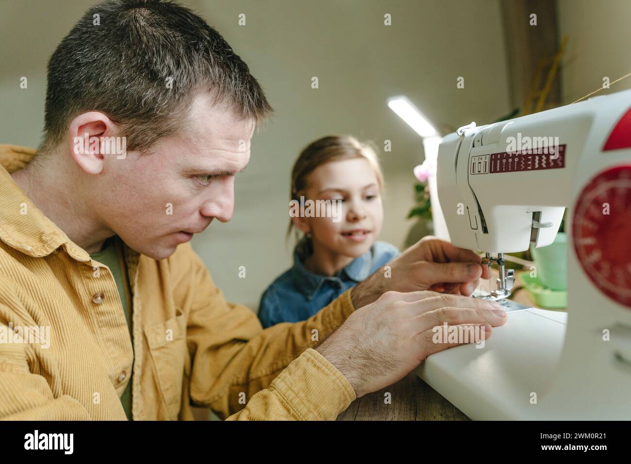 Père concentré mettant du fil sur l'aiguille de machine à coudre à la maison Banque D'Images