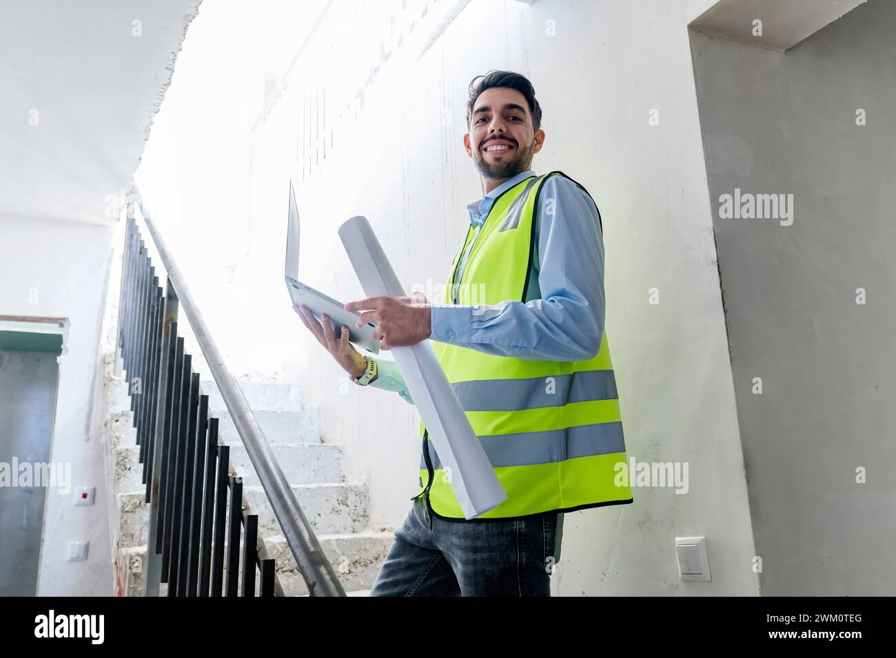 Architecte souriant debout avec plan et ordinateur portable sur le site Banque D'Images