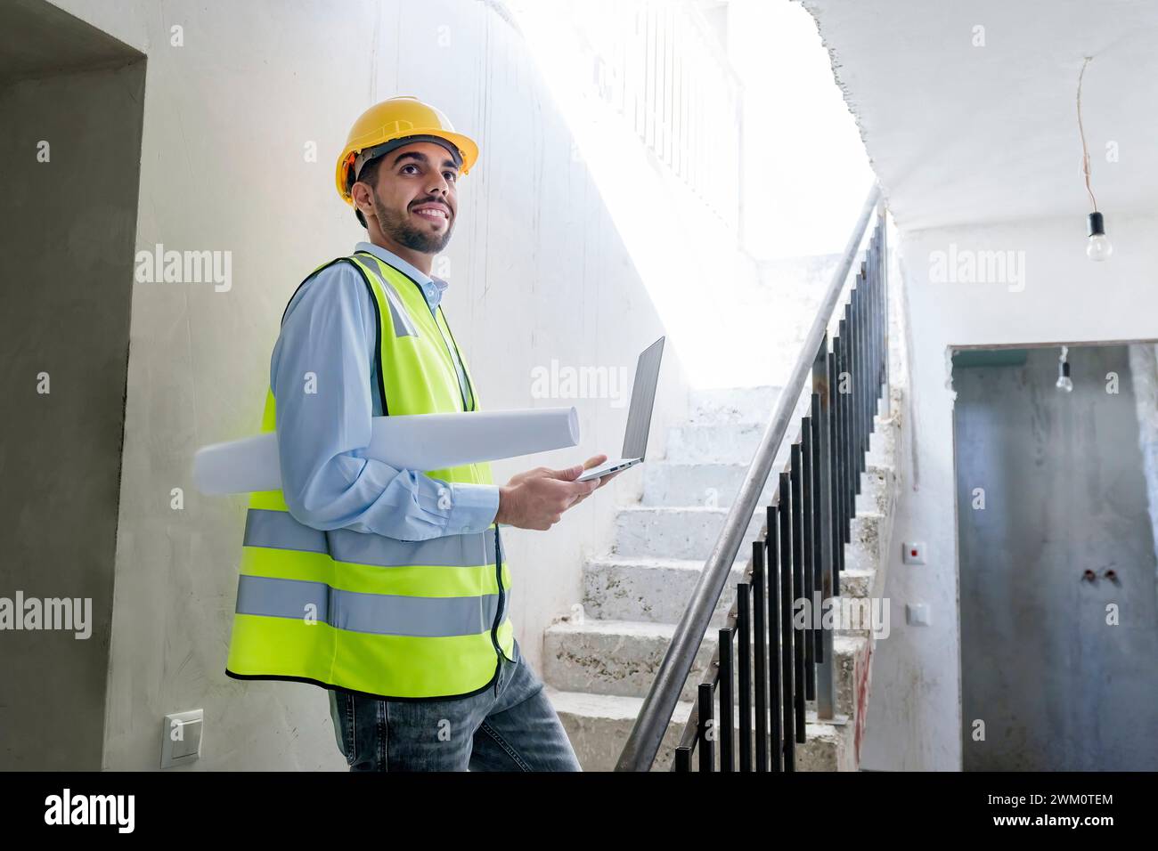 Architecte souriant portant un gilet réfléchissant et debout sur les marches du site Banque D'Images