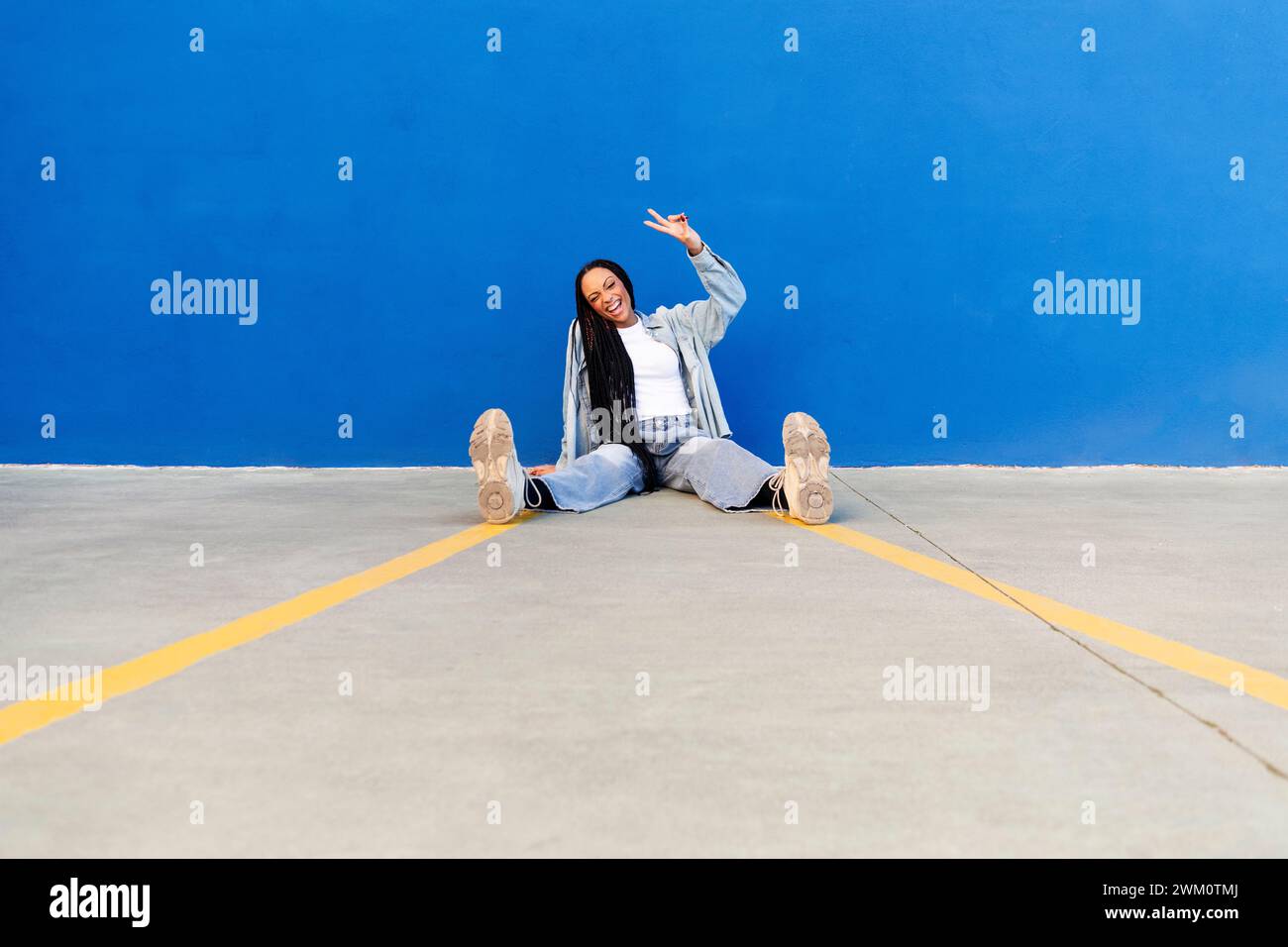 Femme heureuse montrant signe de paix devant le mur bleu Banque D'Images