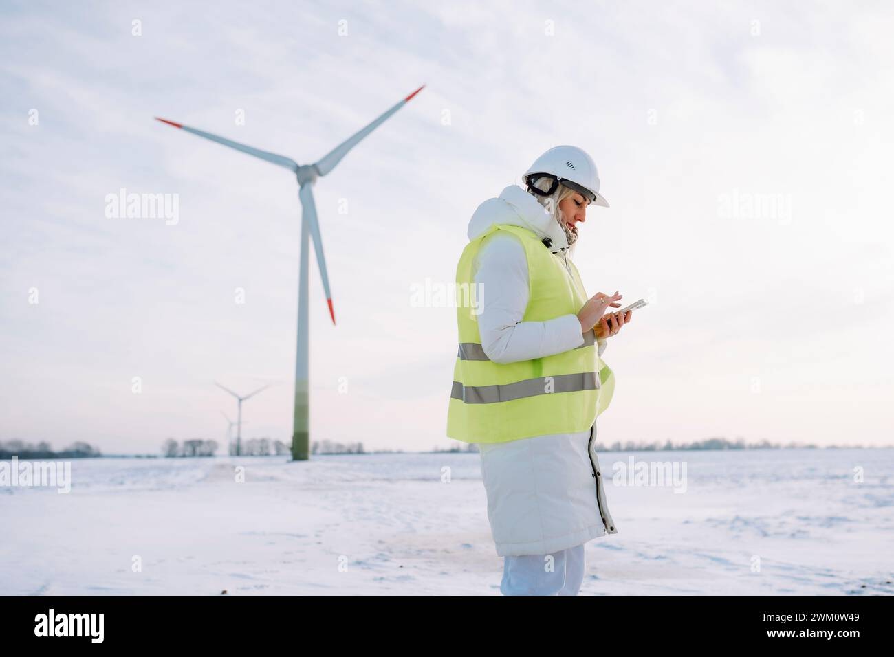 Ingénieur de maintenance utilisant un téléphone intelligent debout devant l'éolienne Banque D'Images