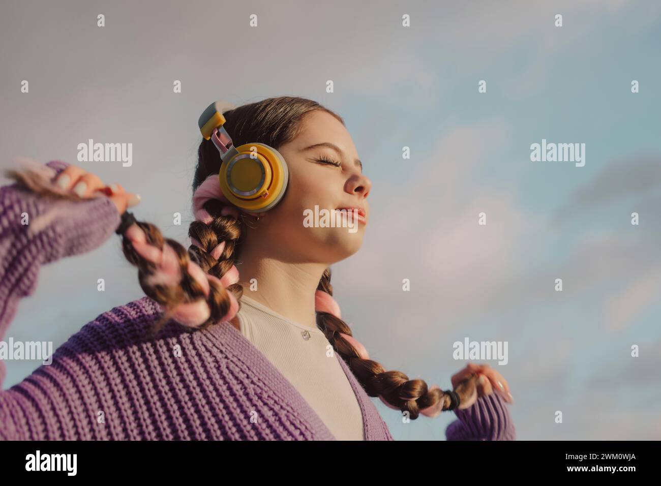 Jeune femme souriante tenant des tresses et écoutant de la musique au coucher du soleil Banque D'Images