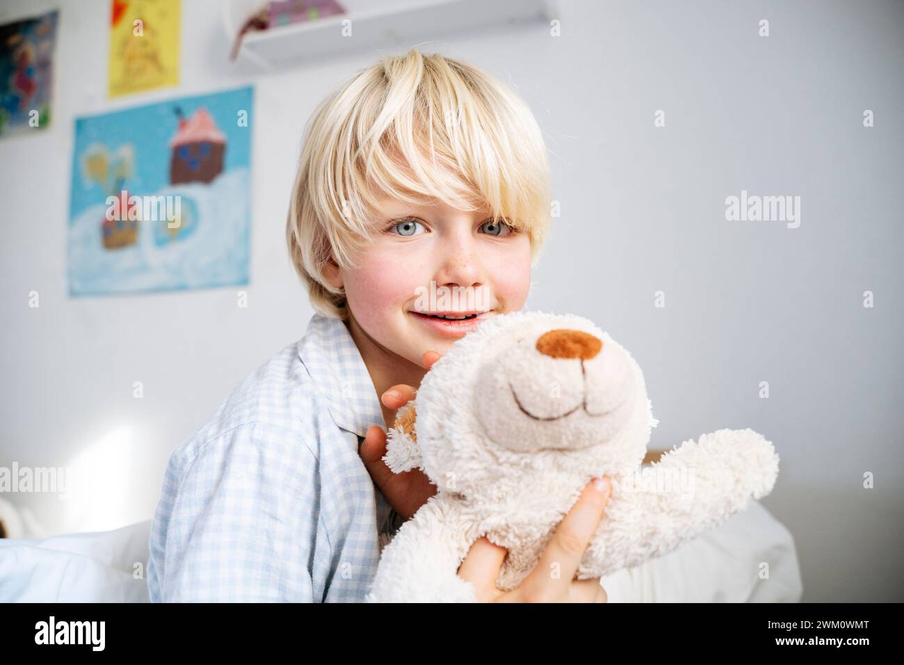 Garçon blond souriant avec ours en peluche à la maison Banque D'Images