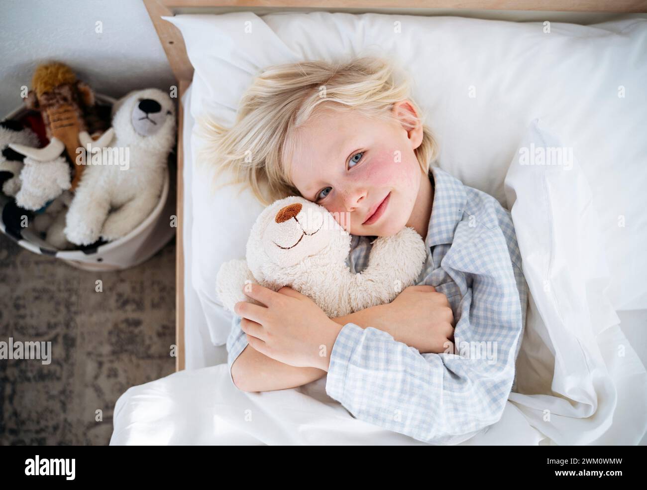 Garçon souriant couché avec un ours en peluche sur le lit à la maison Banque D'Images