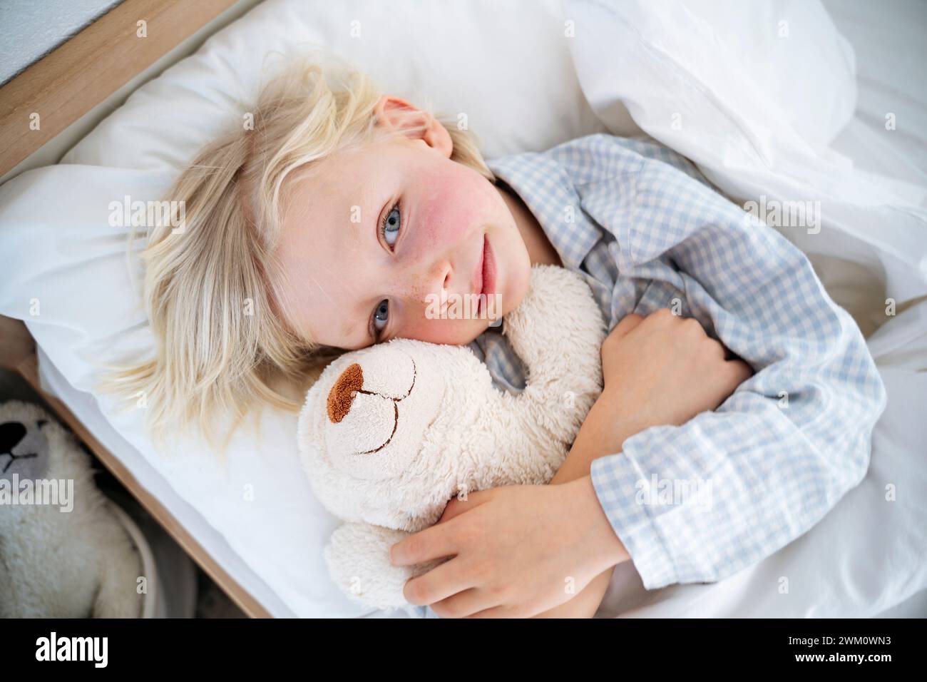 Garçon souriant embrassant ours en peluche sur le lit à la maison Banque D'Images