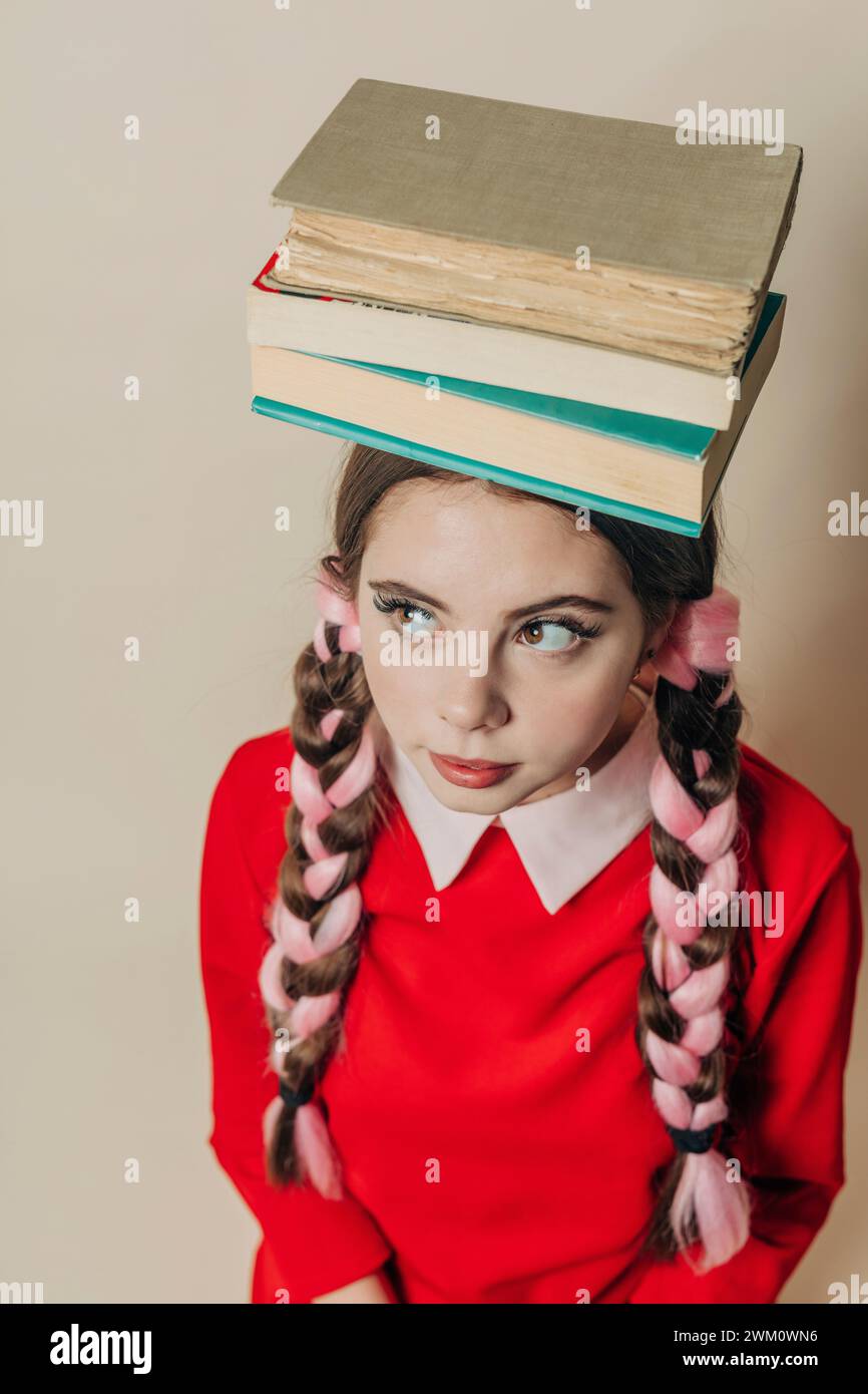 Femme équilibrant des livres sur la tête près du mur Banque D'Images