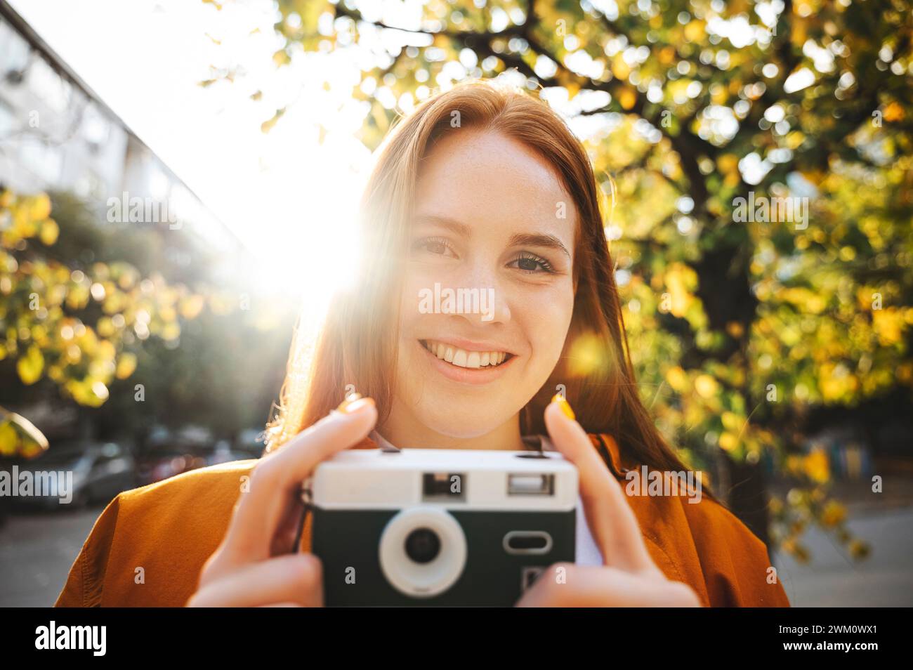 Femme souriante tenant la caméra au jour ensoleillé en automne Banque D'Images