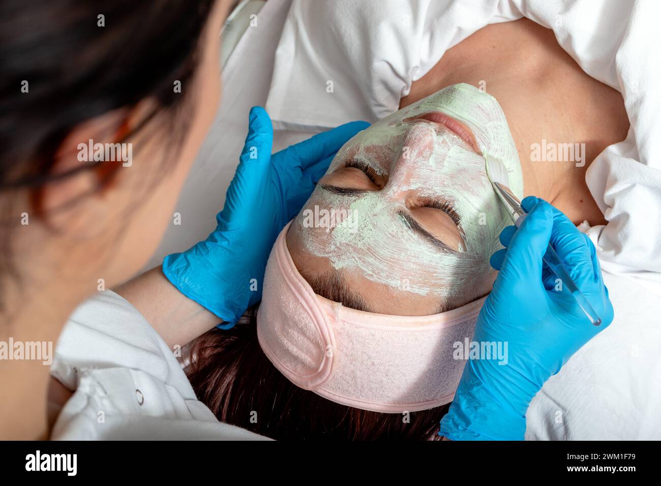 L'esthéticienne applique un masque facial à base de plantes vertes sur le visage du client. Femme d'âge moyen recevant un traitement spa dans un salon de beauté. Banque D'Images