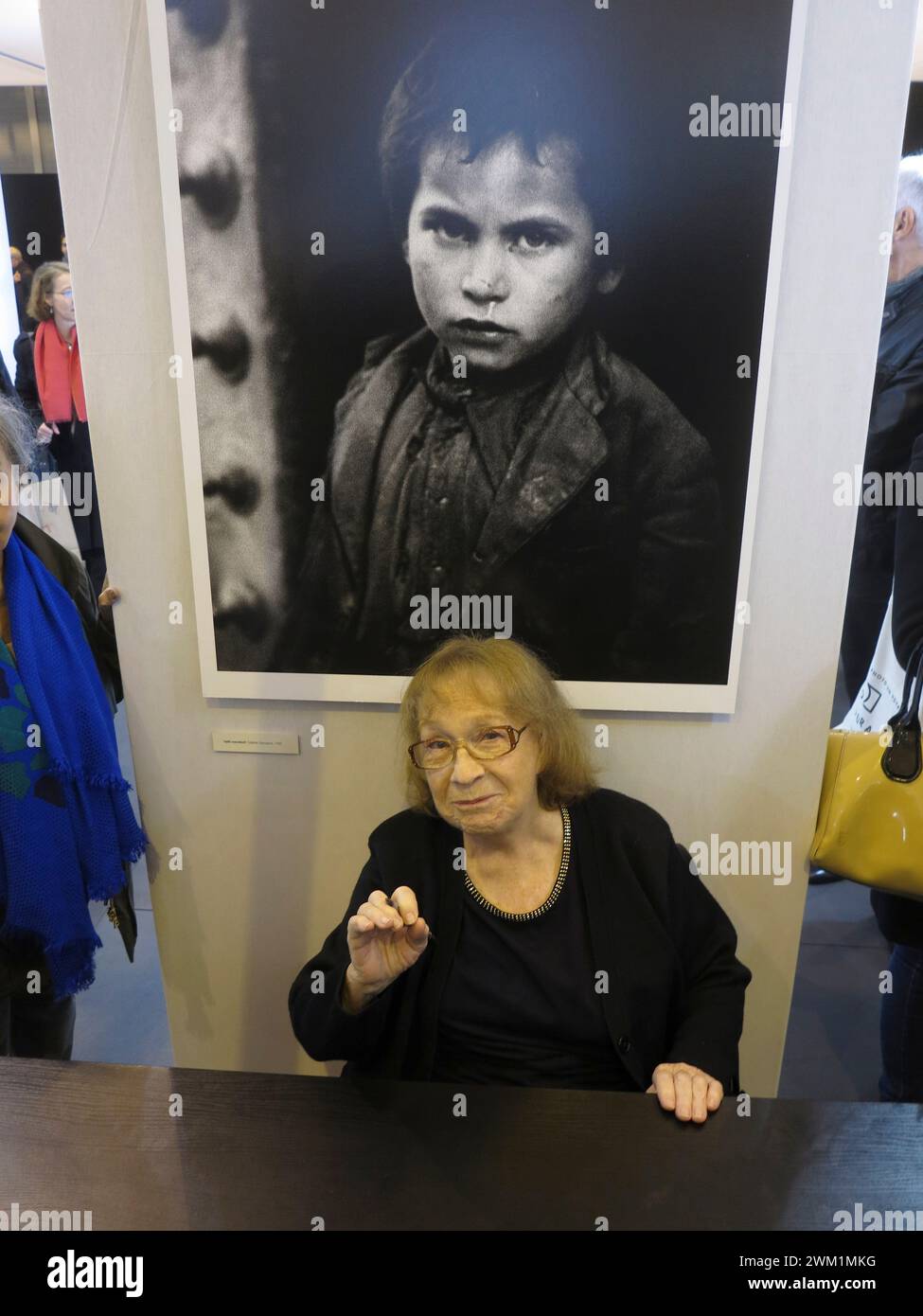 4070630 Paris, novembre 2014, salon de la photo. Sabine Weiss, photographe d'origine franco-suisse, assise devant une de ses œuvres (Little Beggar, Tolède, Espagne, 1950) (photo) ; (add.info.: Paris; Parigi, France ; Francia, Paris Expo porte de Versailles Parigi, novembre 2014, salon de la photo. la fotografa franco-svizzera Sabine Weiss seduta davanti a una sua opera (Piccolo mendicante, Tolède, Spagna, 1952) ; © Marcello Mencarini. Tous droits réservés 2024. Banque D'Images