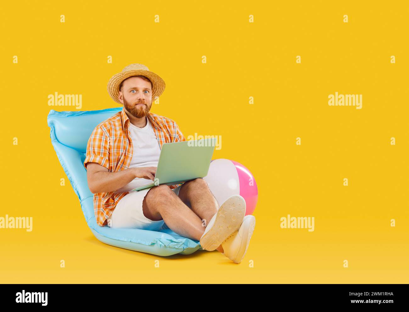 Homme avec ordinateur portable travaillant à distance dans la chaise gonflable de plage sur fond jaune vibrant. Banque D'Images