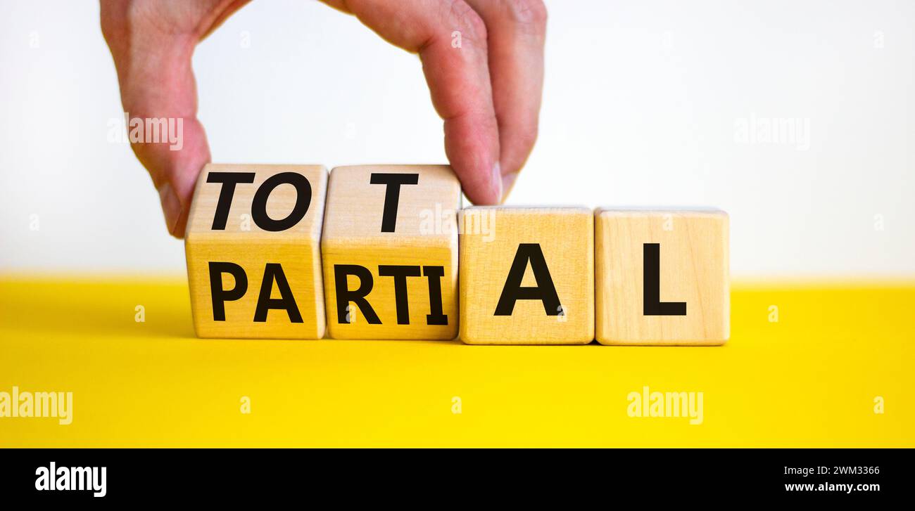 Symbole total ou partiel. Homme d'affaires tourne de beaux cubes en bois et change le mot partiel à Total. Belle table jaune fond blanc. Busi Banque D'Images