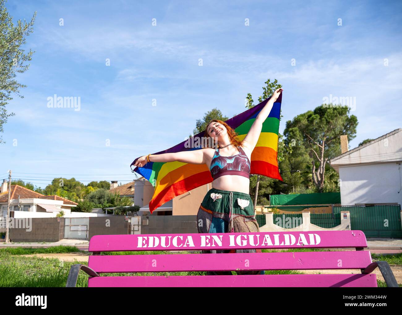 Une jeune femme arbore fièrement un drapeau LGBT alors qu'elle est assise sur un banc Banque D'Images
