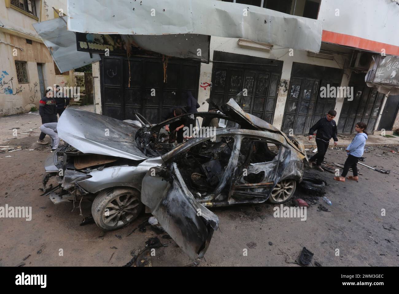 Jenin. 23 février 2024. Les gens se rassemblent autour d’une voiture détruite lors d’une frappe aérienne israélienne dans la ville de Djénine, en Cisjordanie, le 23 février 2024. Le nombre de morts palestiniennes dans la ville de Djénine en Cisjordanie suite à une frappe aérienne israélienne sur un véhicule est passé à deux vendredi, après qu'un garçon de 17 ans a succombé blessé, selon l'agence de presse officielle palestinienne Wafa. Crédit : Nidal Eshtayeh/Xinhua/Alamy Live News Banque D'Images