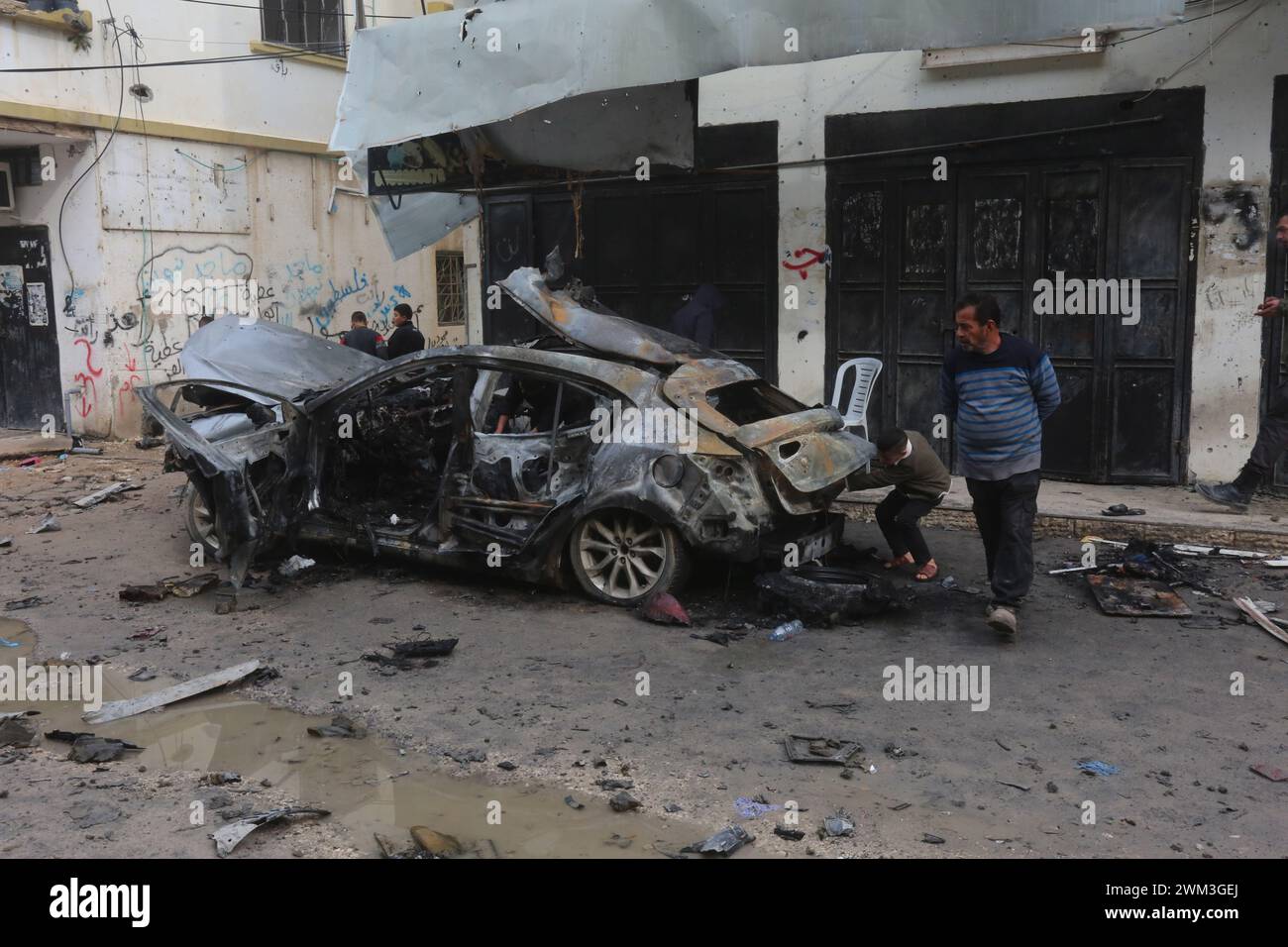 Jenin. 23 février 2024. Les gens inspectent une voiture détruite lors d’une frappe aérienne israélienne dans la ville de Djénine en Cisjordanie, le 23 février 2024. Le nombre de morts palestiniennes dans la ville de Djénine en Cisjordanie suite à une frappe aérienne israélienne sur un véhicule est passé à deux vendredi, après qu'un garçon de 17 ans a succombé blessé, selon l'agence de presse officielle palestinienne Wafa. Crédit : Nidal Eshtayeh/Xinhua/Alamy Live News Banque D'Images