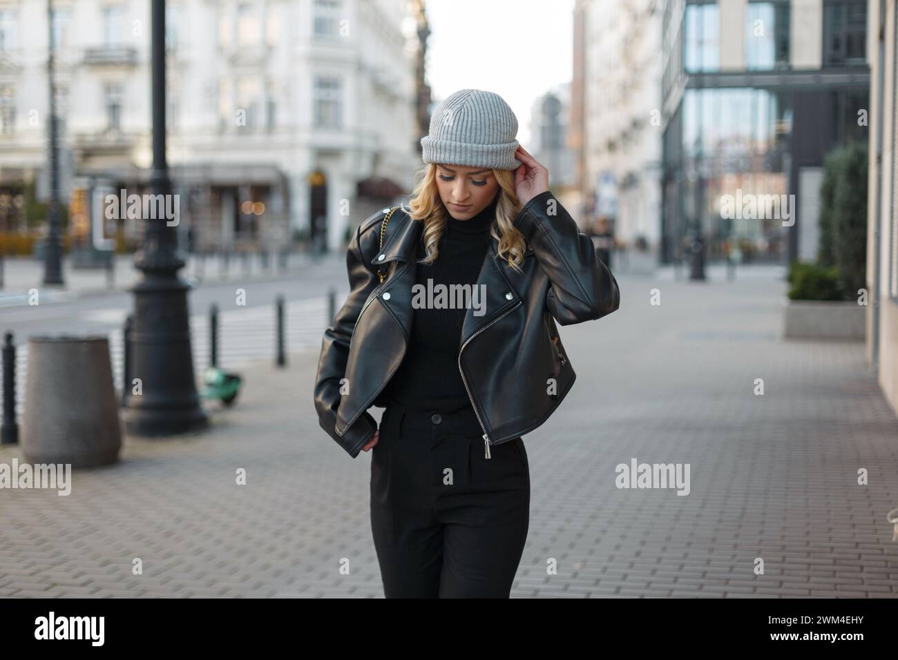 belle jeune femme élégante dans des vêtements noirs de mode avec un chapeau tricoté et veste en cuir se promène dans la ville Banque D'Images