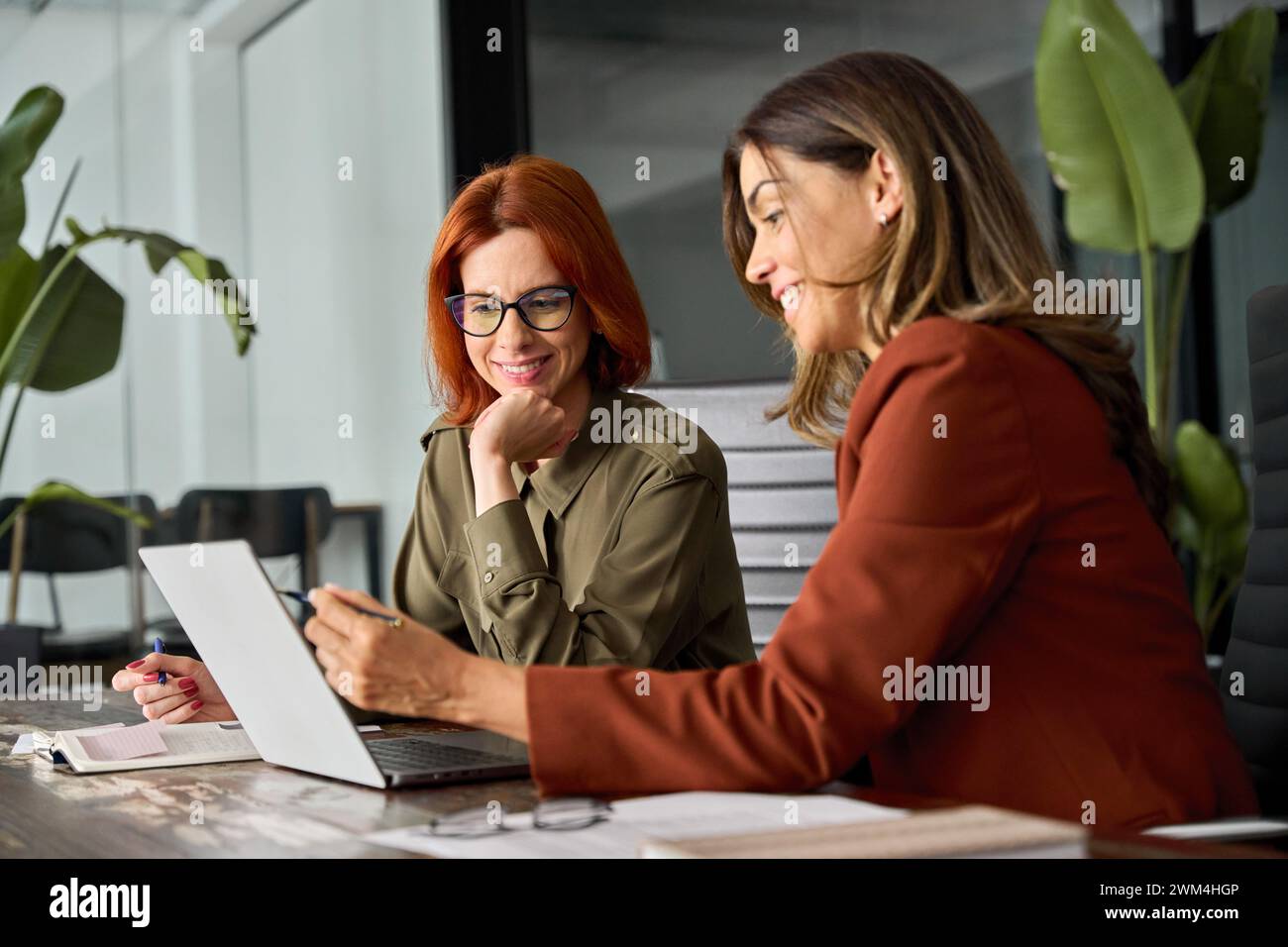 Deux collègues féminines occupées heureuses travaillant ensemble en utilisant l'ordinateur au bureau dans le bureau. Banque D'Images