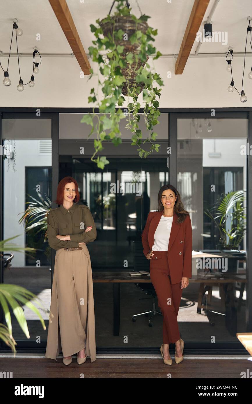 Deux joyeuses femmes d'affaires souriantes debout au travail dans le bureau. Portrait vertical. Banque D'Images