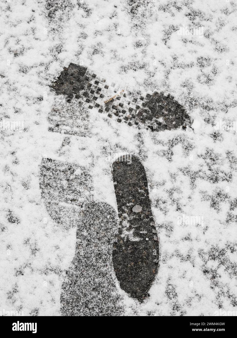 Une paire d'empreintes de pas laisse une marque sur une couverture de neige fraîchement tombée couvrant une rue à Gothenburg, capturant un moment solitaire un jour d'hiver. Banque D'Images