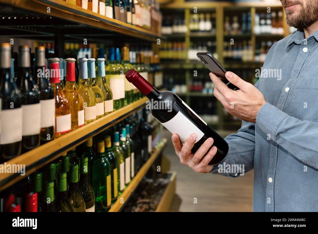 Homme consommateur de détail scanner l'étiquette électronique de la bouteille de vin avec son téléphone intelligent dans le magasin d'alcool. Banque D'Images