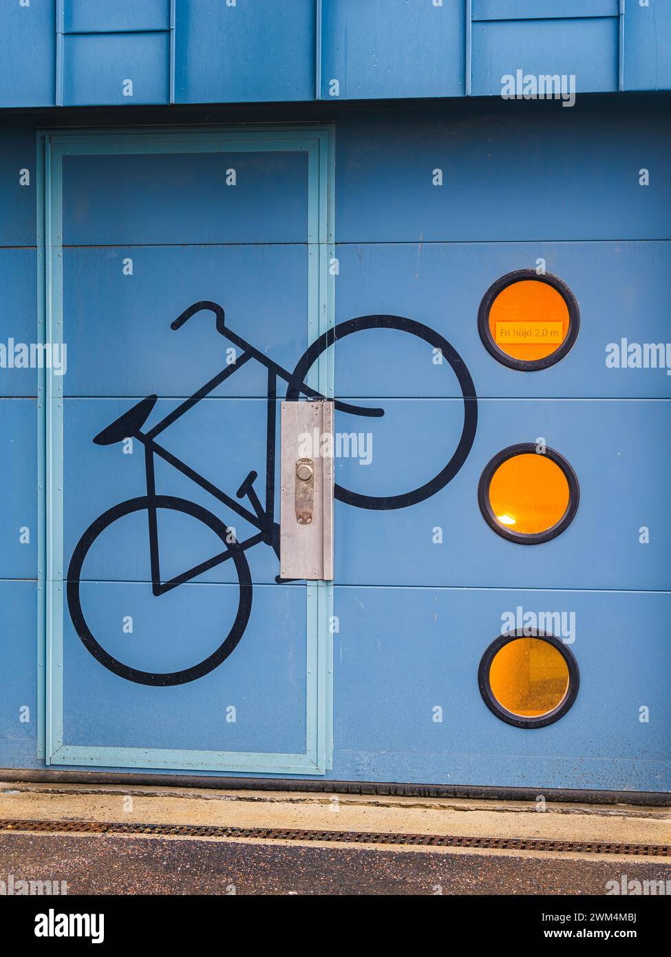 Un mur d'entrepôt bleu vif à Gothenburg, en Suède, présente une silhouette peinte d'un vélo et trois panneaux circulaires orange. Le dessin sugg Banque D'Images