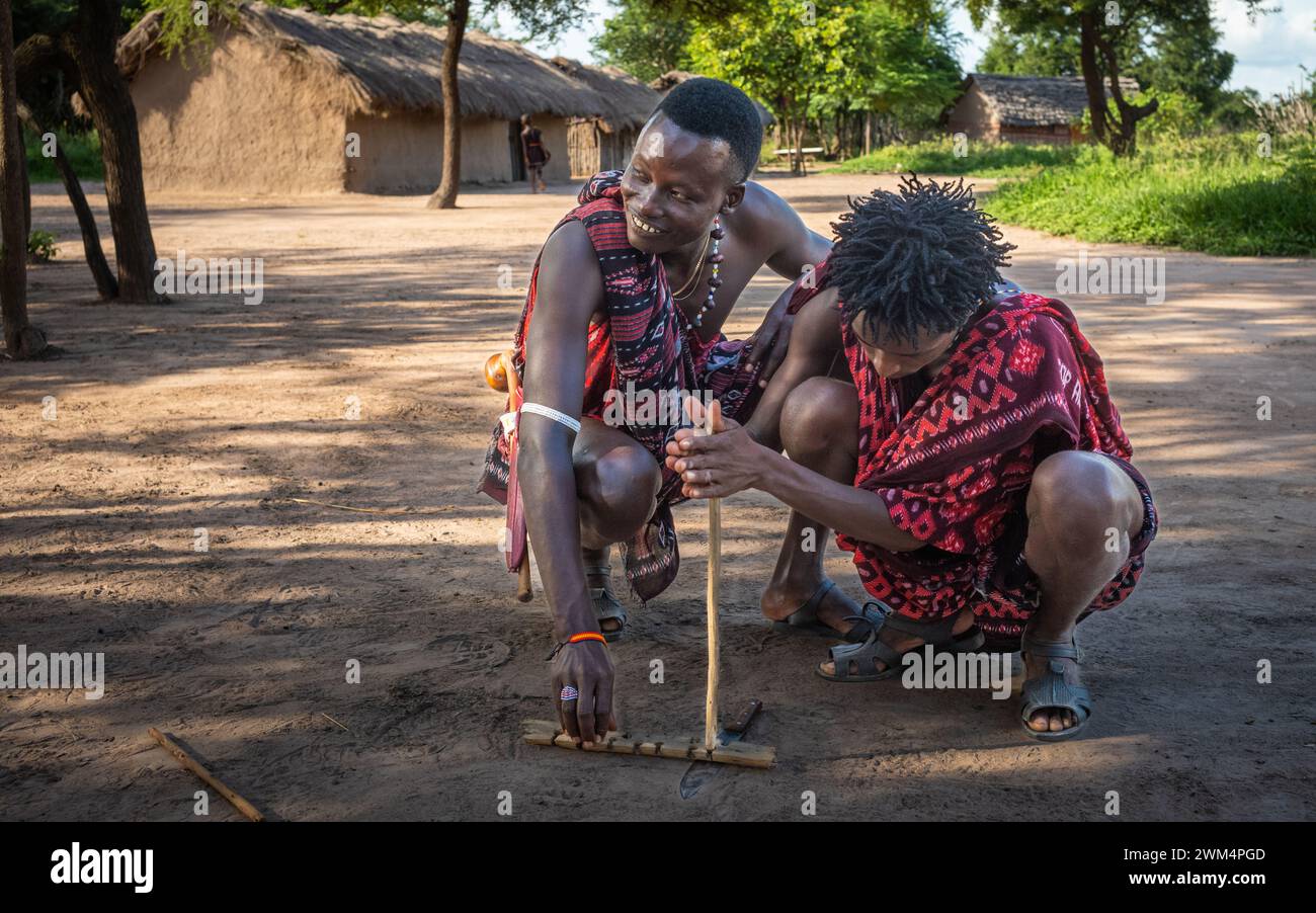 Deux guerriers Massaï utilisent la friction en frottant des bâtons ensemble pour allumer un incendie dans un village de Mikumi, en Tanzanie. Banque D'Images