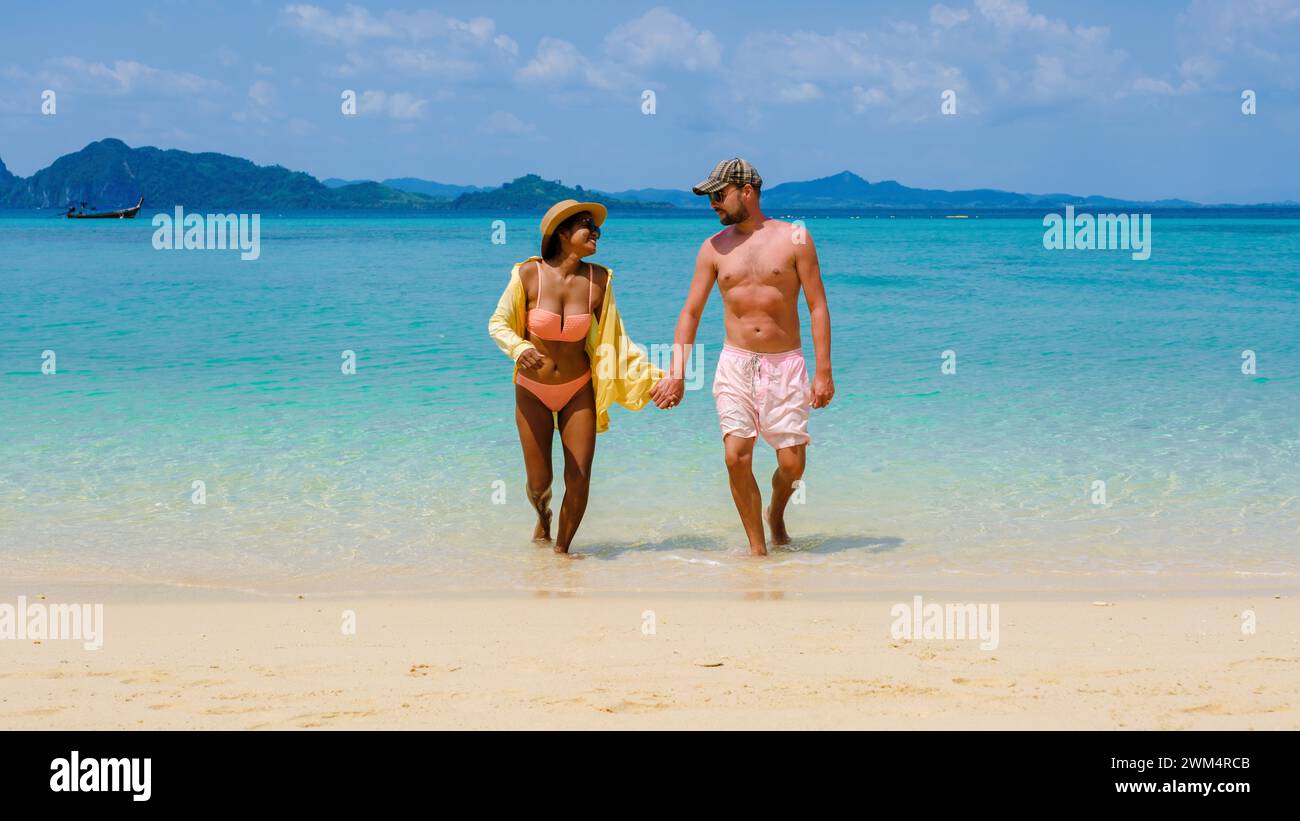 Un couple diversifié d'hommes et de femmes marchant de l'océan à la plage de l'île de Koh Kradan en Thaïlande, des hommes caucasiens, et des femmes asiatiques vacances d'été, voyageant autour de la Thaïlande Banque D'Images
