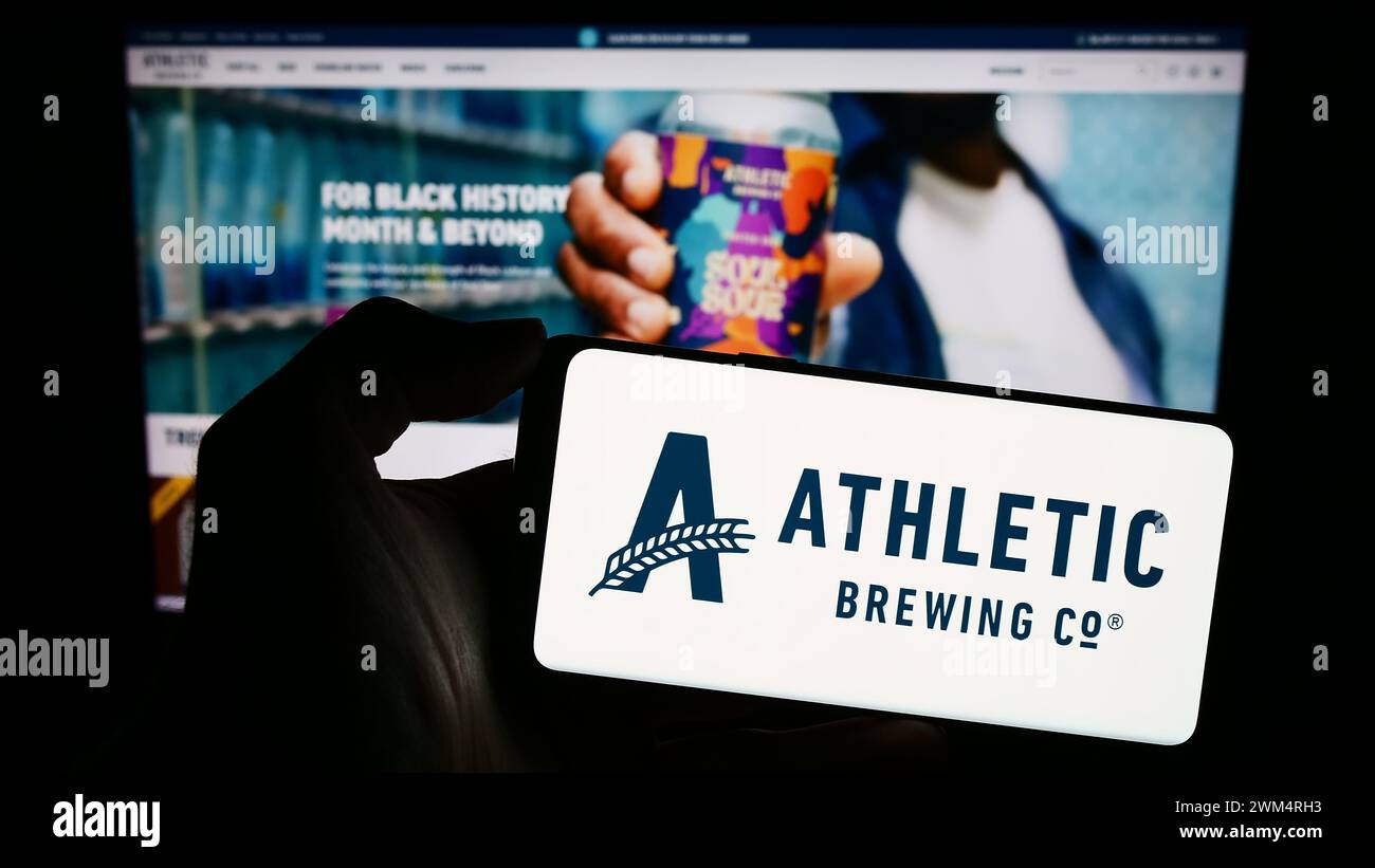 Personne tenant le téléphone portable avec le logo de la société américaine de boissons Athletic Brewing Company en face de la page Web. Concentrez-vous sur l'affichage du téléphone. Banque D'Images