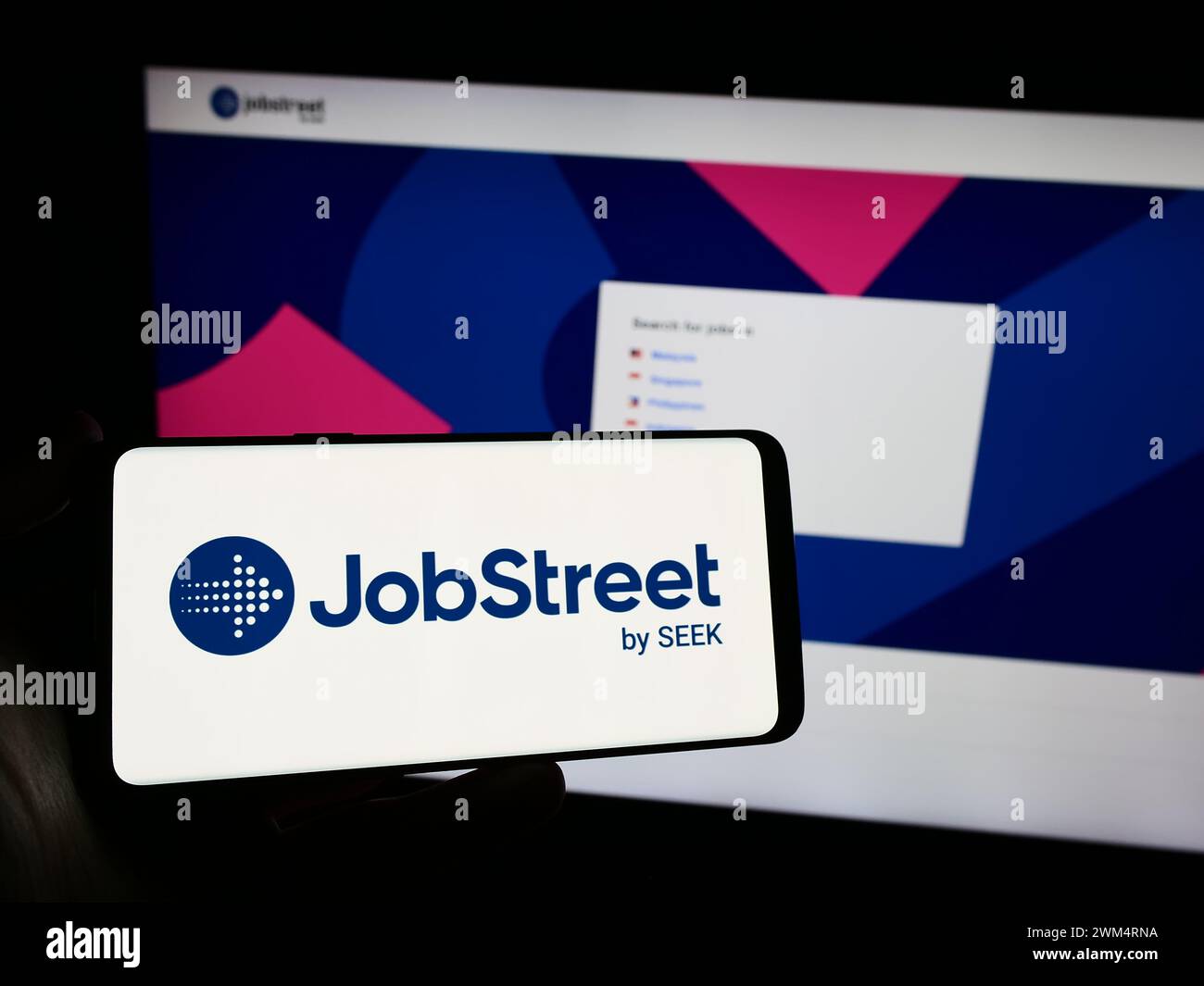 Personne tenant un smartphone avec le logo de la société de plate-forme d'emploi Jobstreet en face du site Web. Concentrez-vous sur l'affichage du téléphone. Banque D'Images