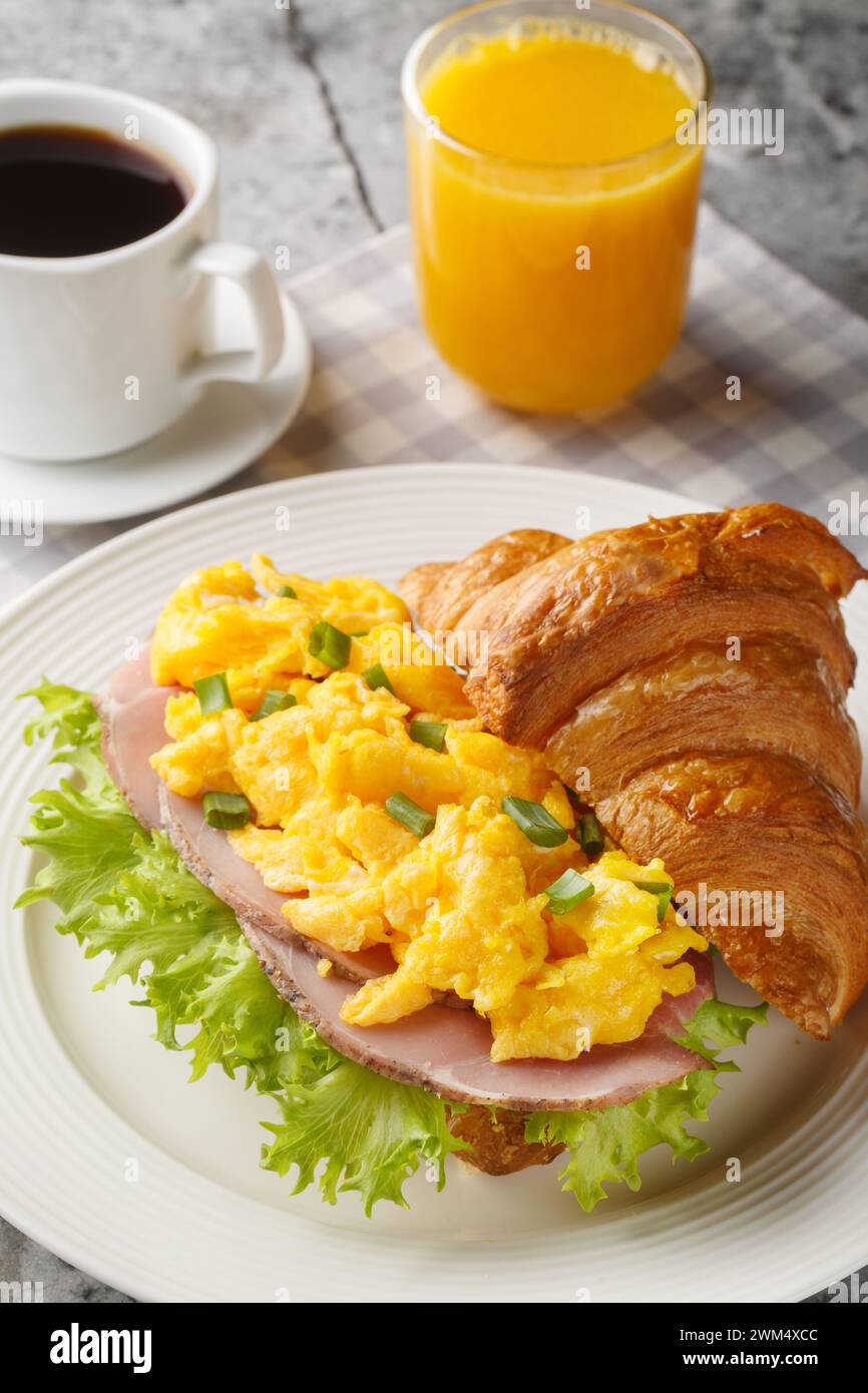 Croissant de jambon aux œufs brouillés servi avec du jus d'orange et du café en gros plan sur une table en marbre. Vertical Banque D'Images