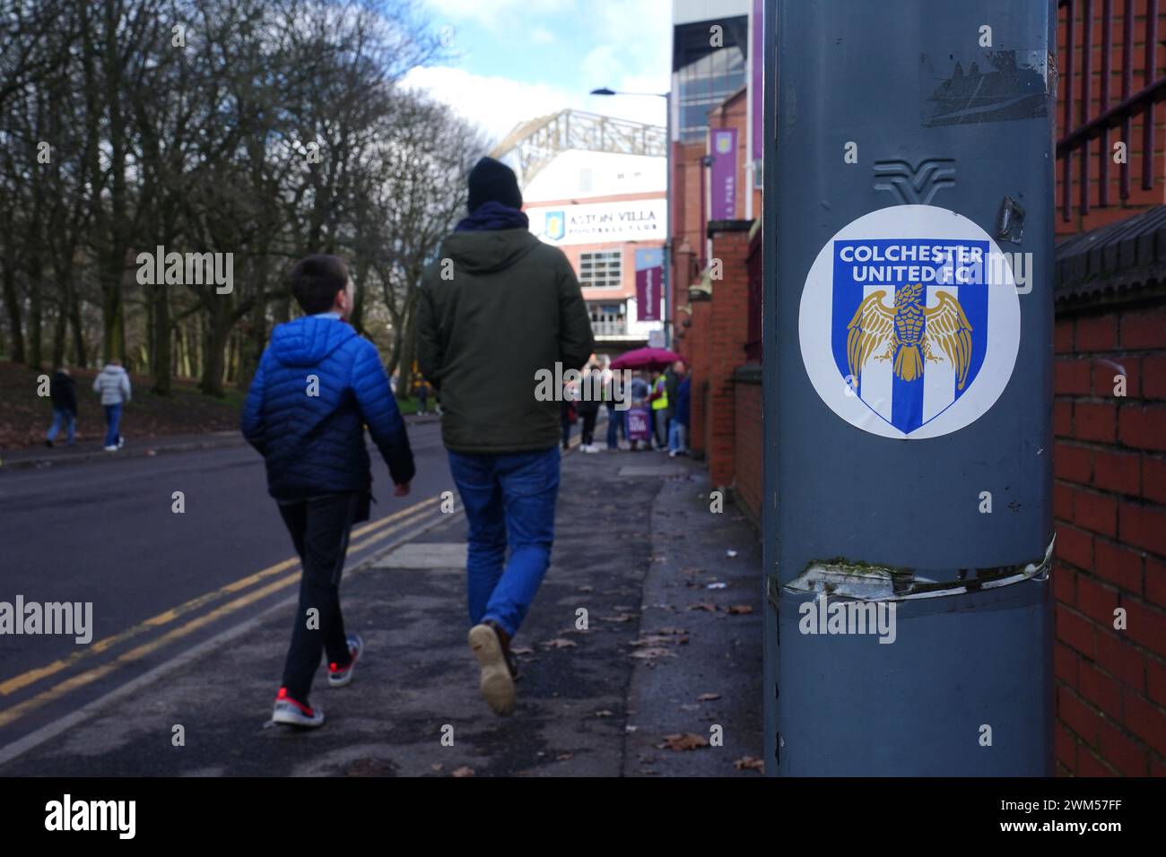Les fans passent devant un grand autocollant Colchester United FC alors qu'ils se dirigent vers le stade avant le match de premier League à Villa Park, Birmingham. Date de la photo : samedi 24 février 2024. Banque D'Images
