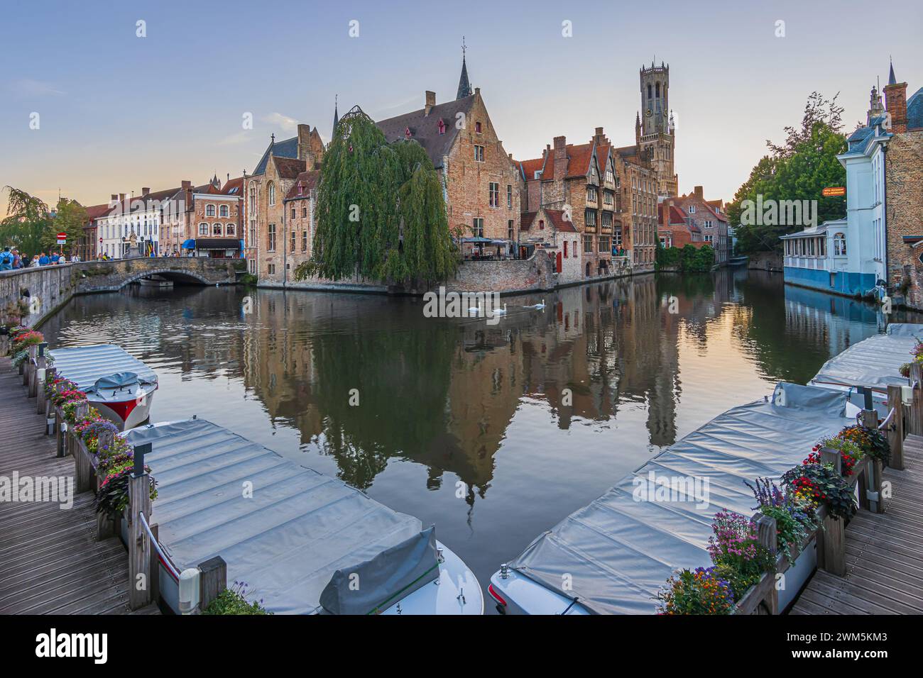 Ambiance du soir au coucher du soleil sur le canal du Rosaire Quay dans la vieille ville de Bruges avec des bateaux sur la jetée. Maisons de marchands historiques et bâtiments anciens Banque D'Images