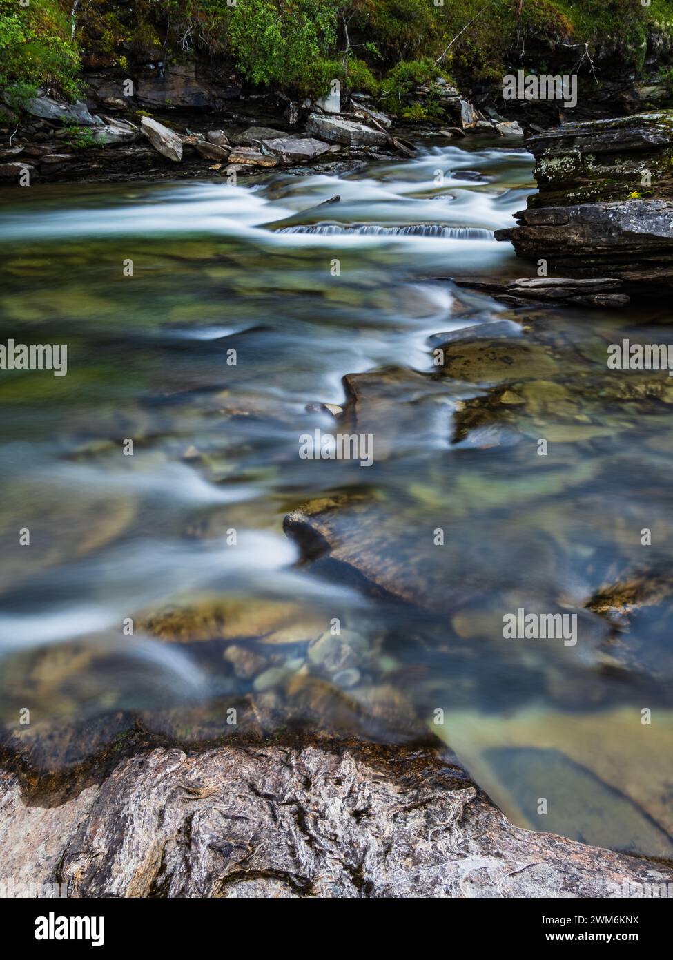 La paisible rivière Ljusnan serpente à travers le paysage accidenté de Härjedalen, son eau cascadant sur des rochers et des galets. La lumière tamisée et douce Banque D'Images