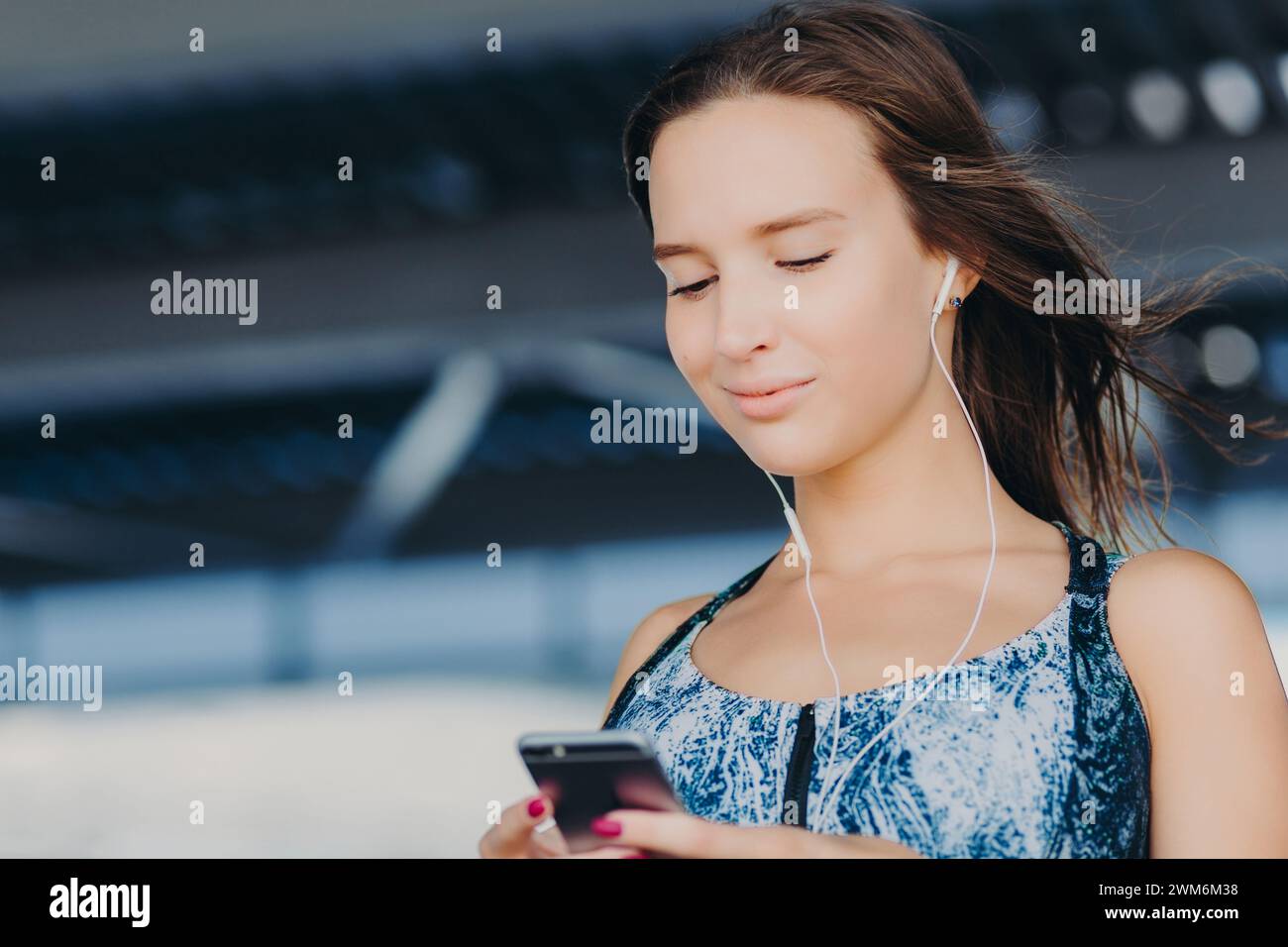 Femme de contenu avec des écouteurs profitant d'un appareil intelligent sur une passerelle urbaine. Banque D'Images