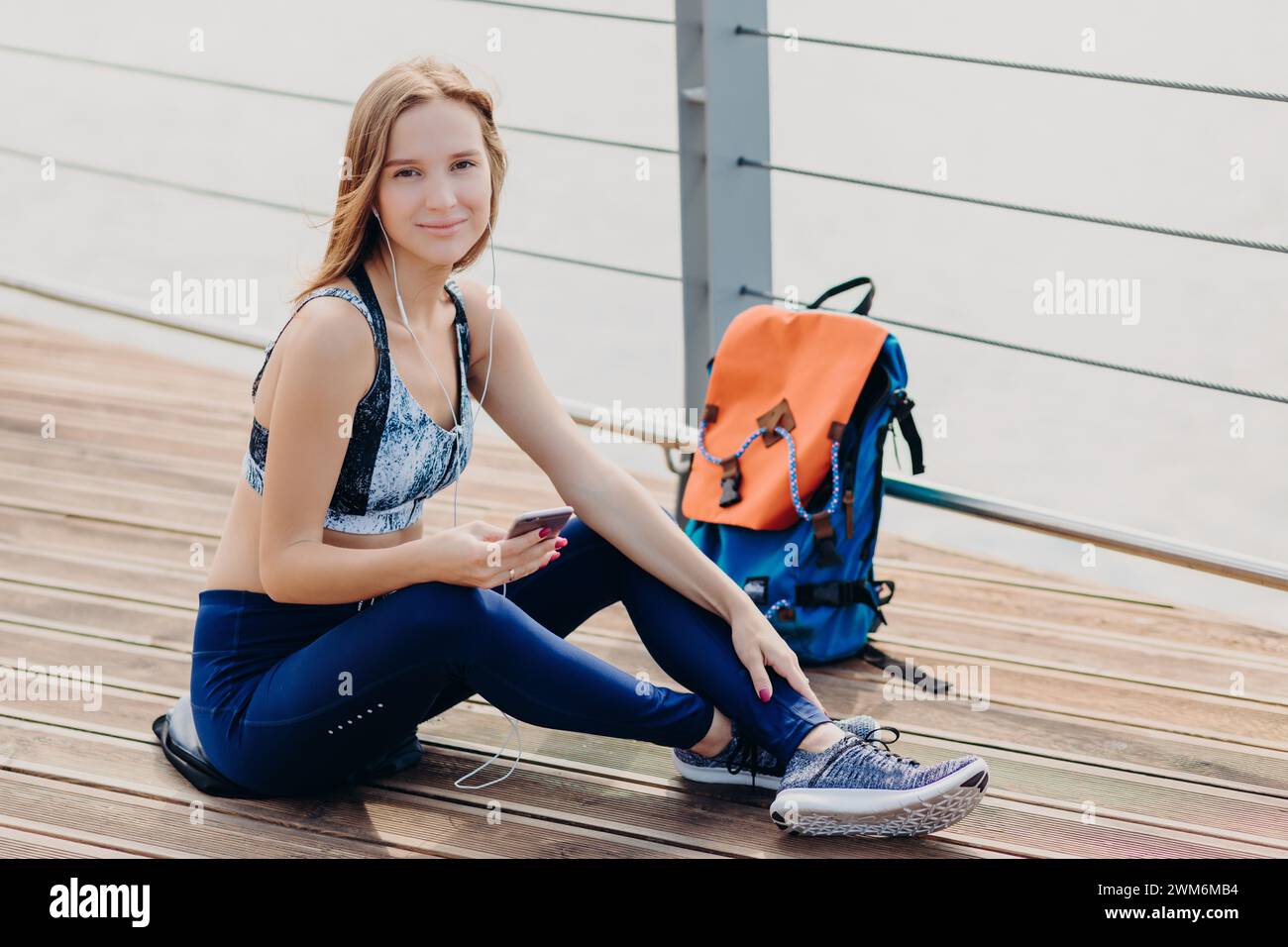 Femme axée sur le fitness vérifie son téléphone tout en se reposant près d'une rivière de la ville. Banque D'Images