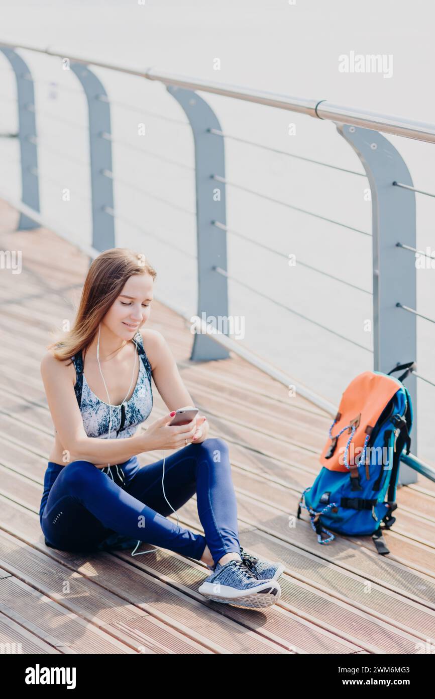 Femme détendue avec des écouteurs sur une promenade en bord de mer en utilisant son téléphone portable. Banque D'Images