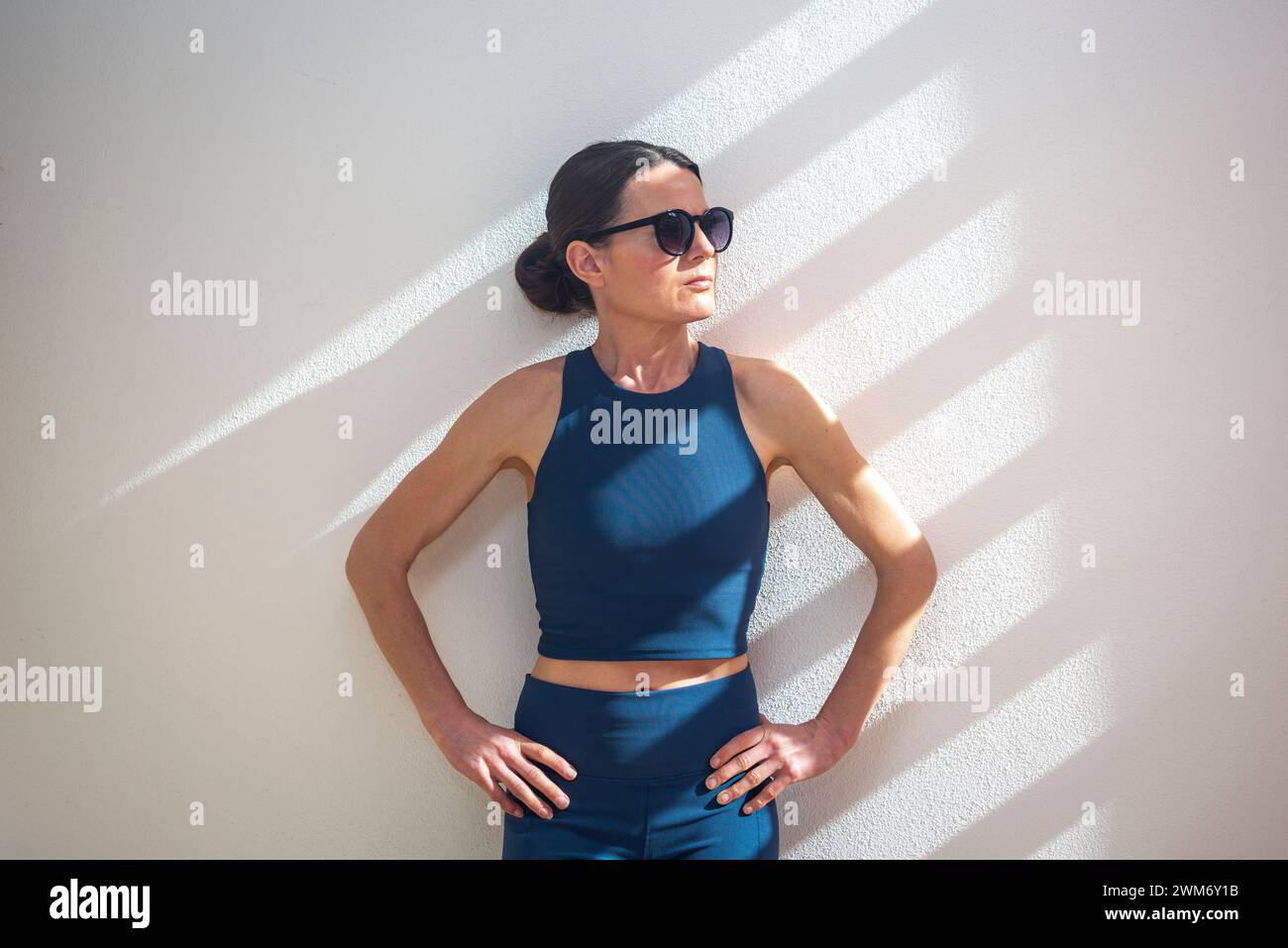 femme sportive debout contre un mur au soleil, portant des lunettes de soleil. Banque D'Images femme sportive debout contre un mur au soleil, portant des lunettes de soleil. Banque D'Images