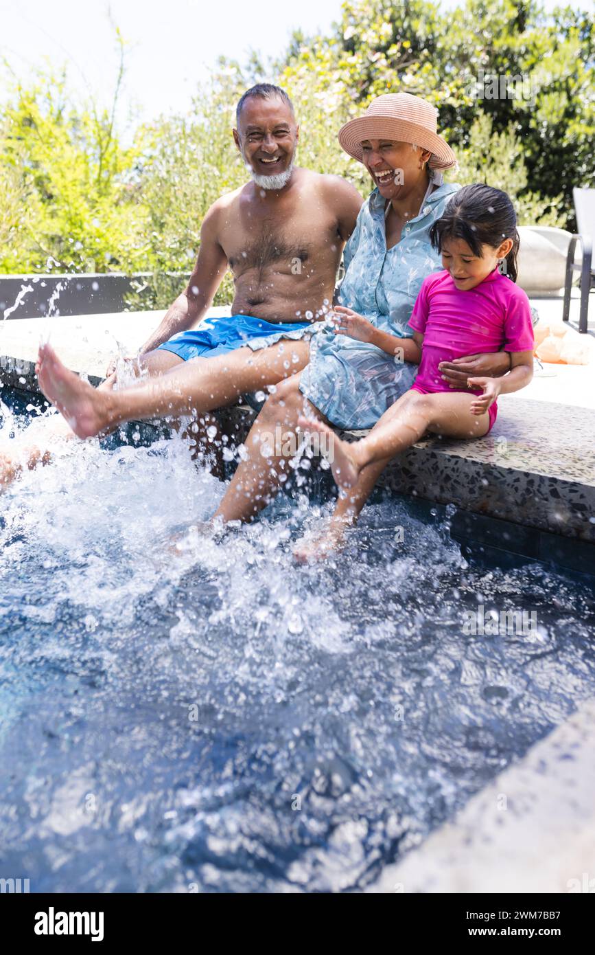 Les grands-parents biraciaux et la petite-fille profitent d'une journée ensoleillée au bord de la piscine avec espace de copie Banque D'Images