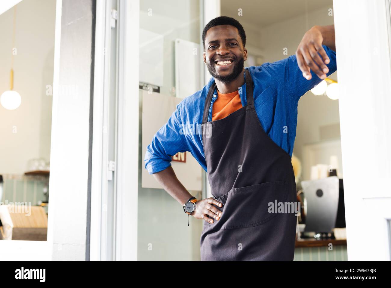 Homme afro-américain dans un tablier se tient à l'entrée d'un café avec un espace de copie Banque D'Images